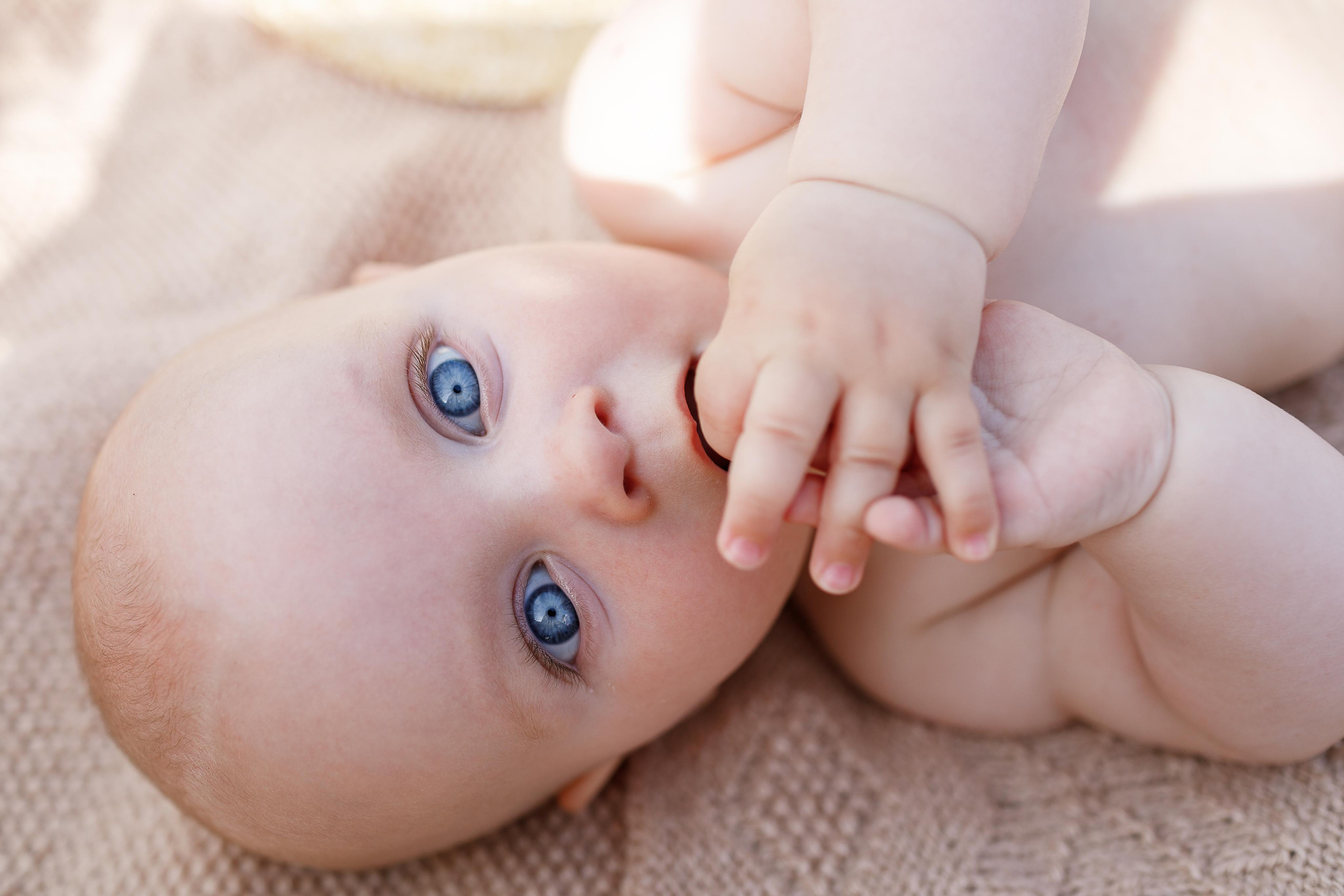 Ребенок с большими голубыми глазами лёжа на спине смотрит на небо. 