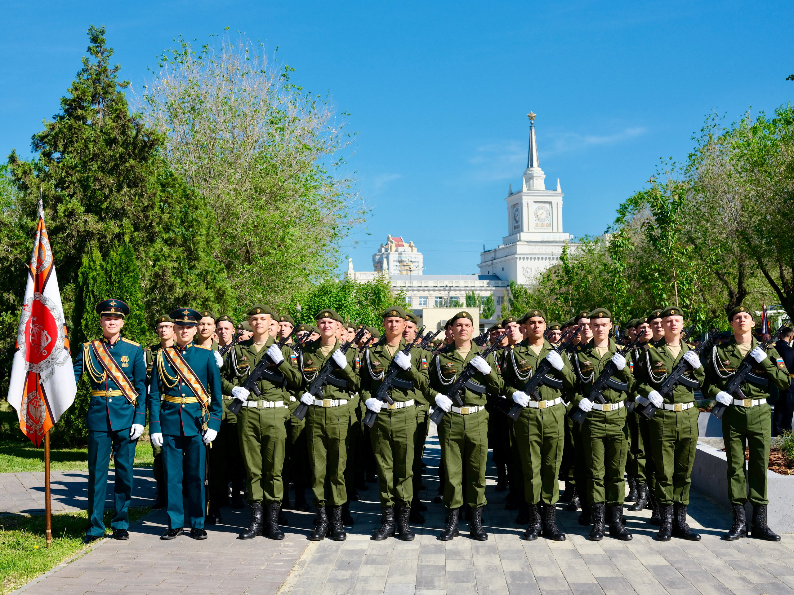 Музыкальный оркестр военных морских пехотинцев в парадной форме играет марш на фоне трибун с флагами России и Волгоградской области