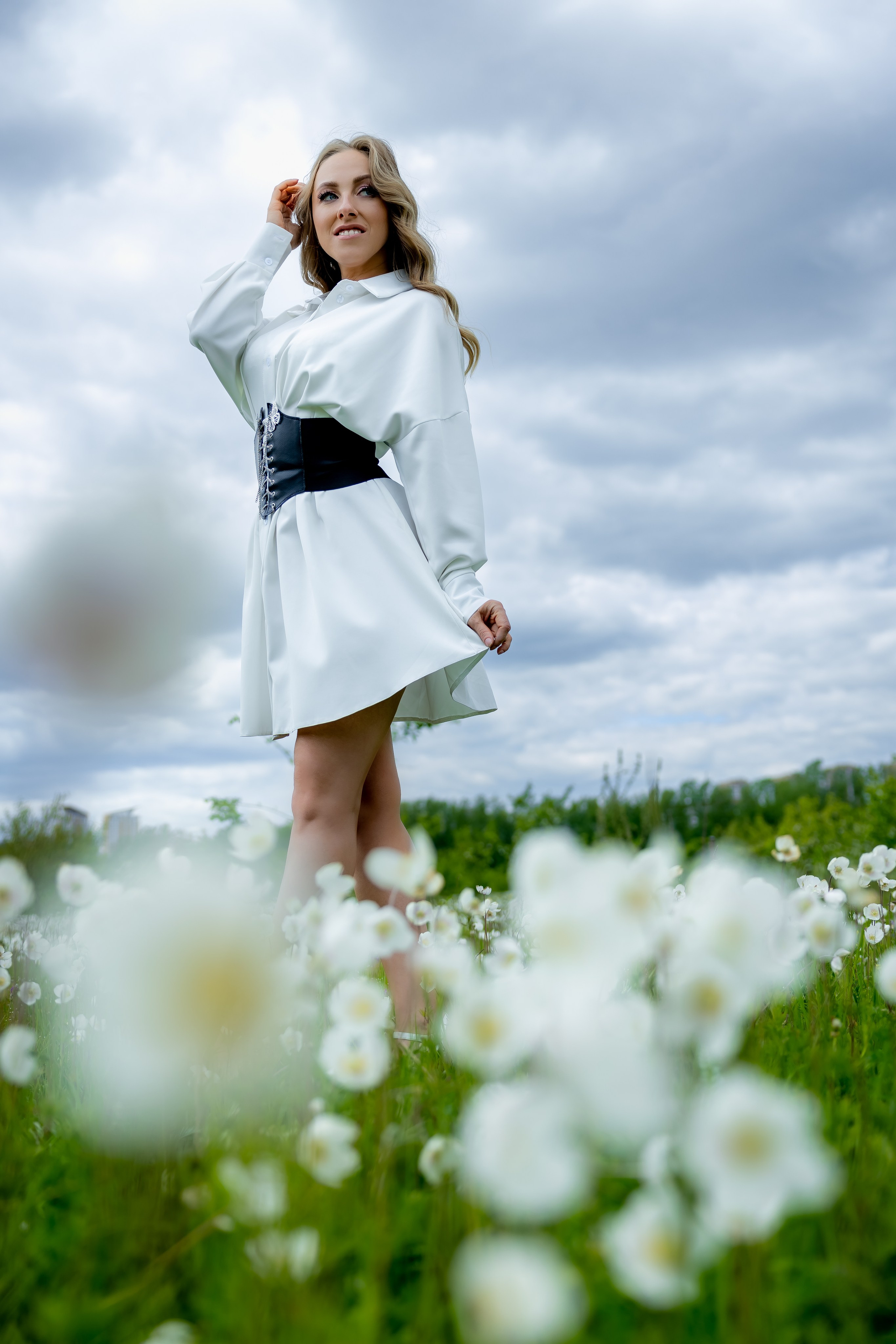 Женщина в белом платье на фоне цветущего поля и облачного неба