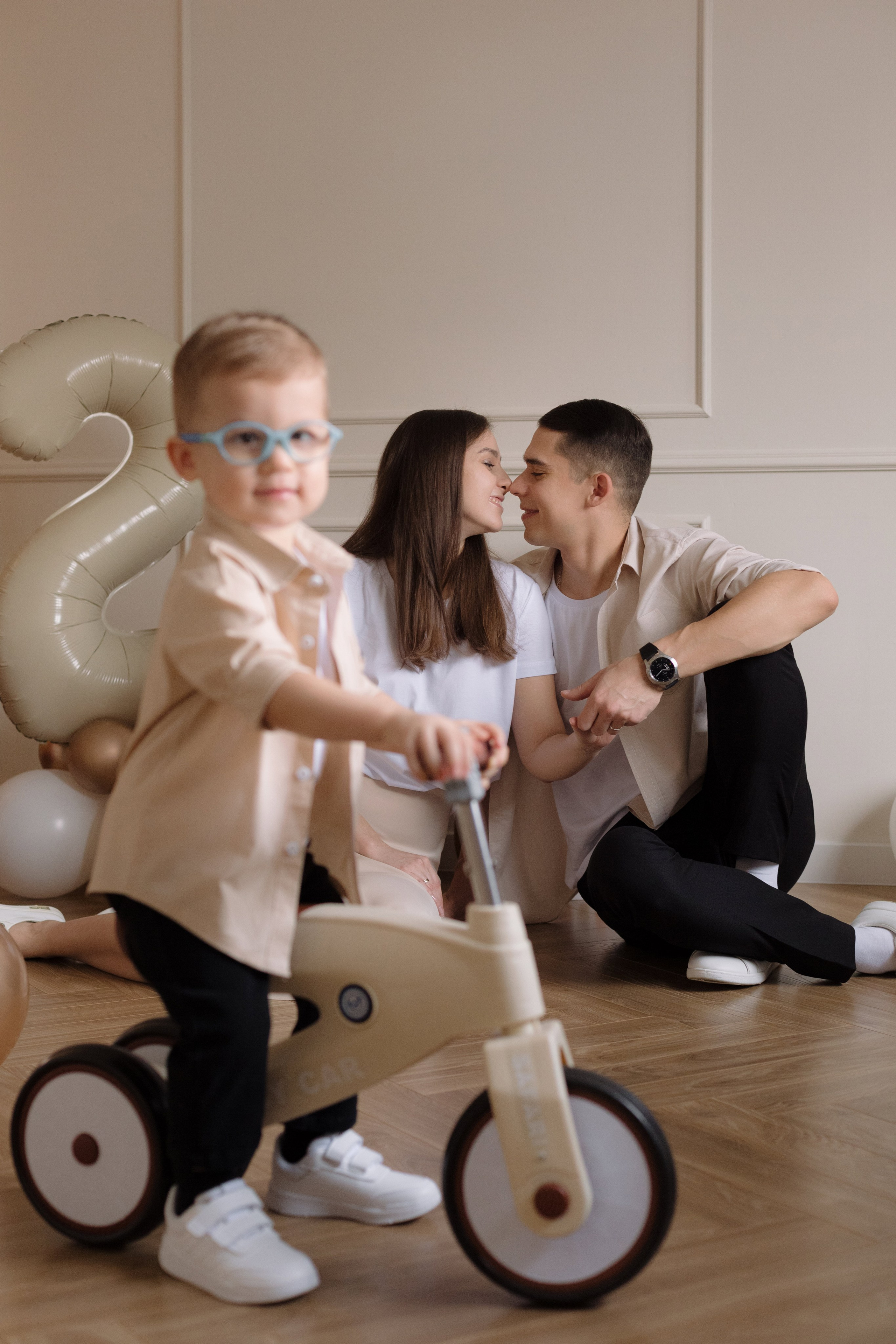Фотосессия в Таганроге в студии — ребёнок на беговеле на переднем плане, родители на фоне, семейная съёмка