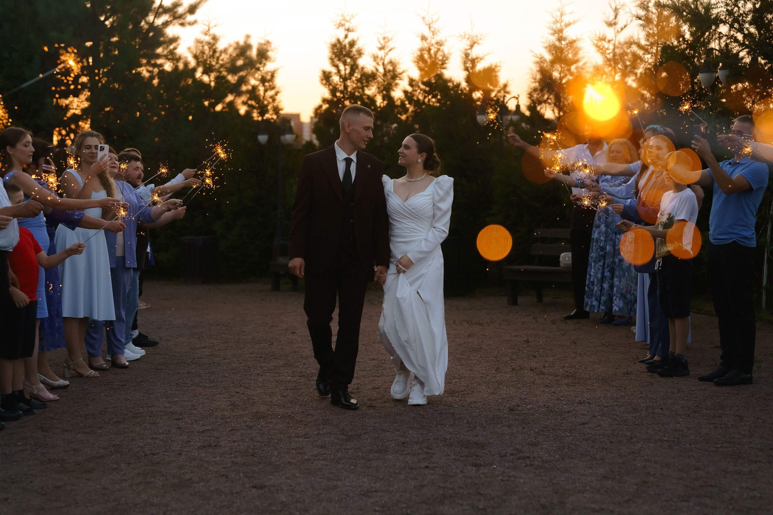 Пара проходит через коридор бенгальских огней после церемонии — тёплый вечерний момент