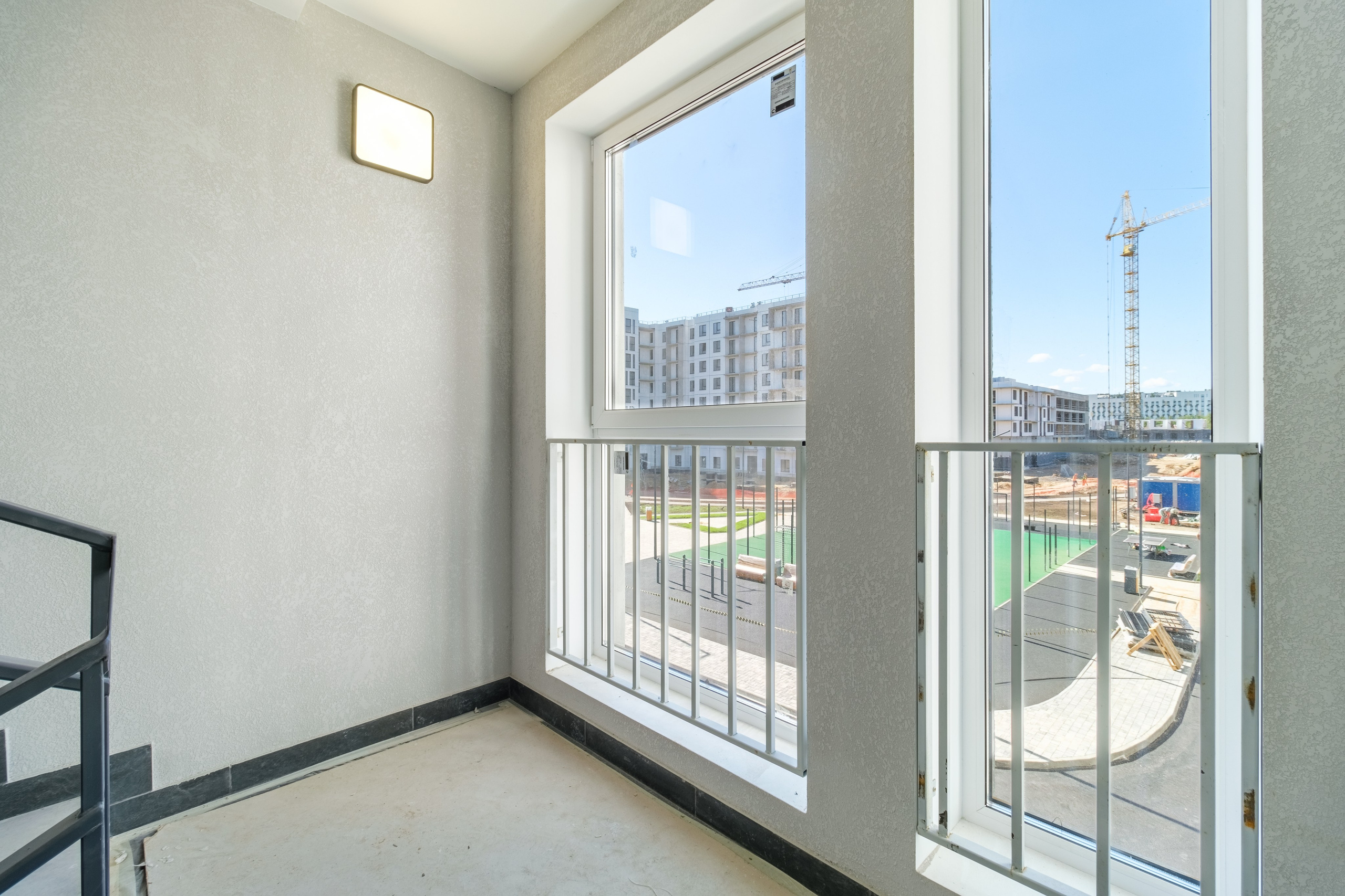 Лестница жилого комплекса с большими окнами от пола до потолка с видом на благоустроенный двор.