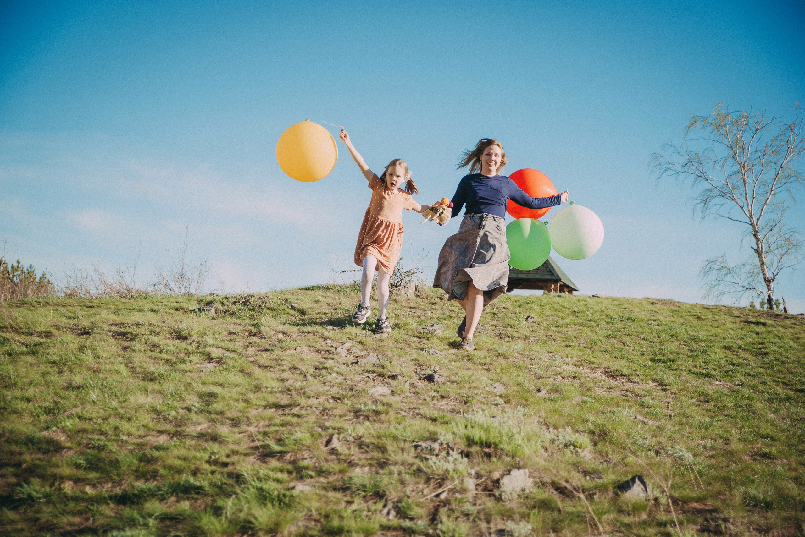 счастливые мама и дочка бегут с горы размахивая шарами