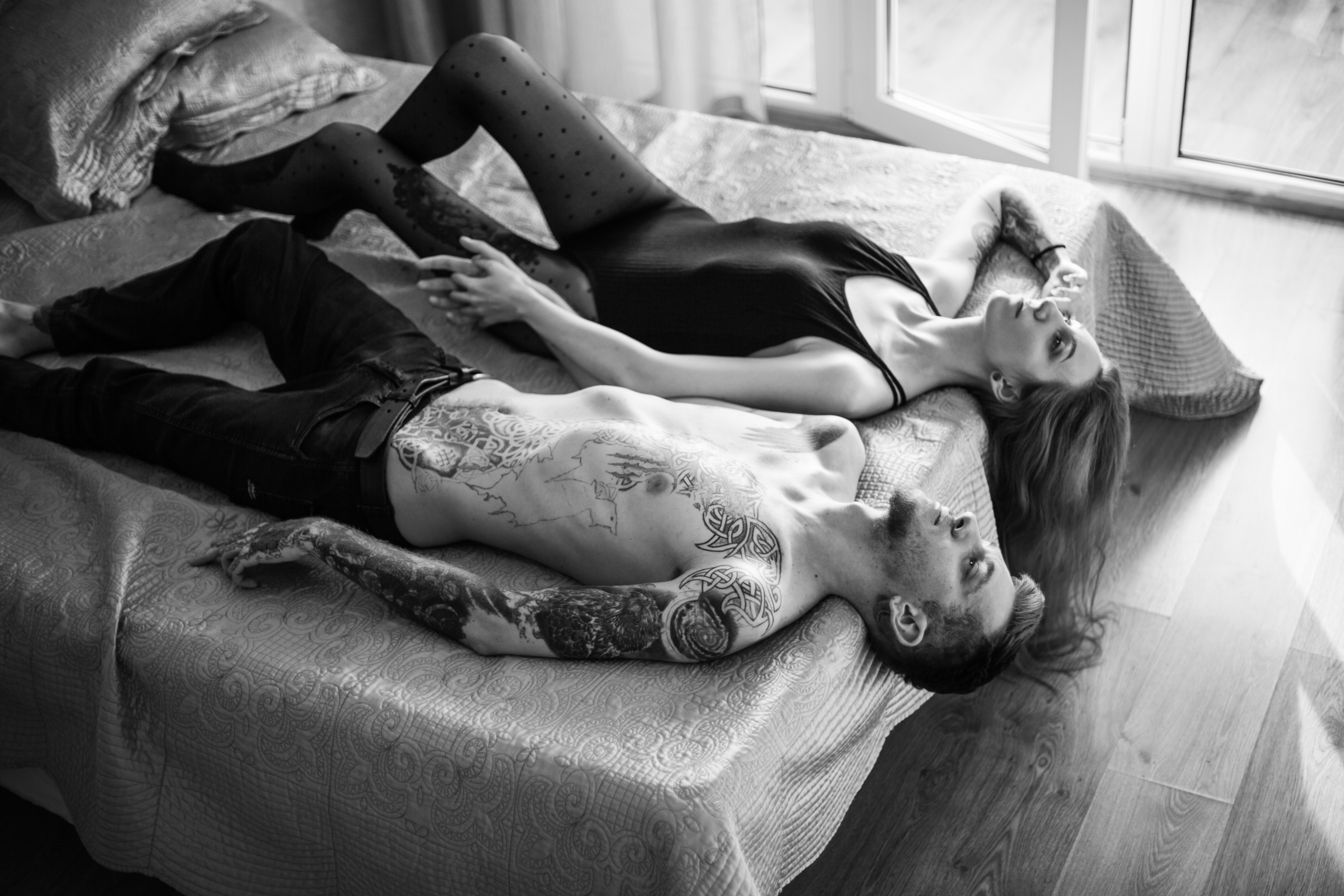 Черно-белый портрет Love story, красивая пара в татуировках  лежит на кровати, взявшись за руки