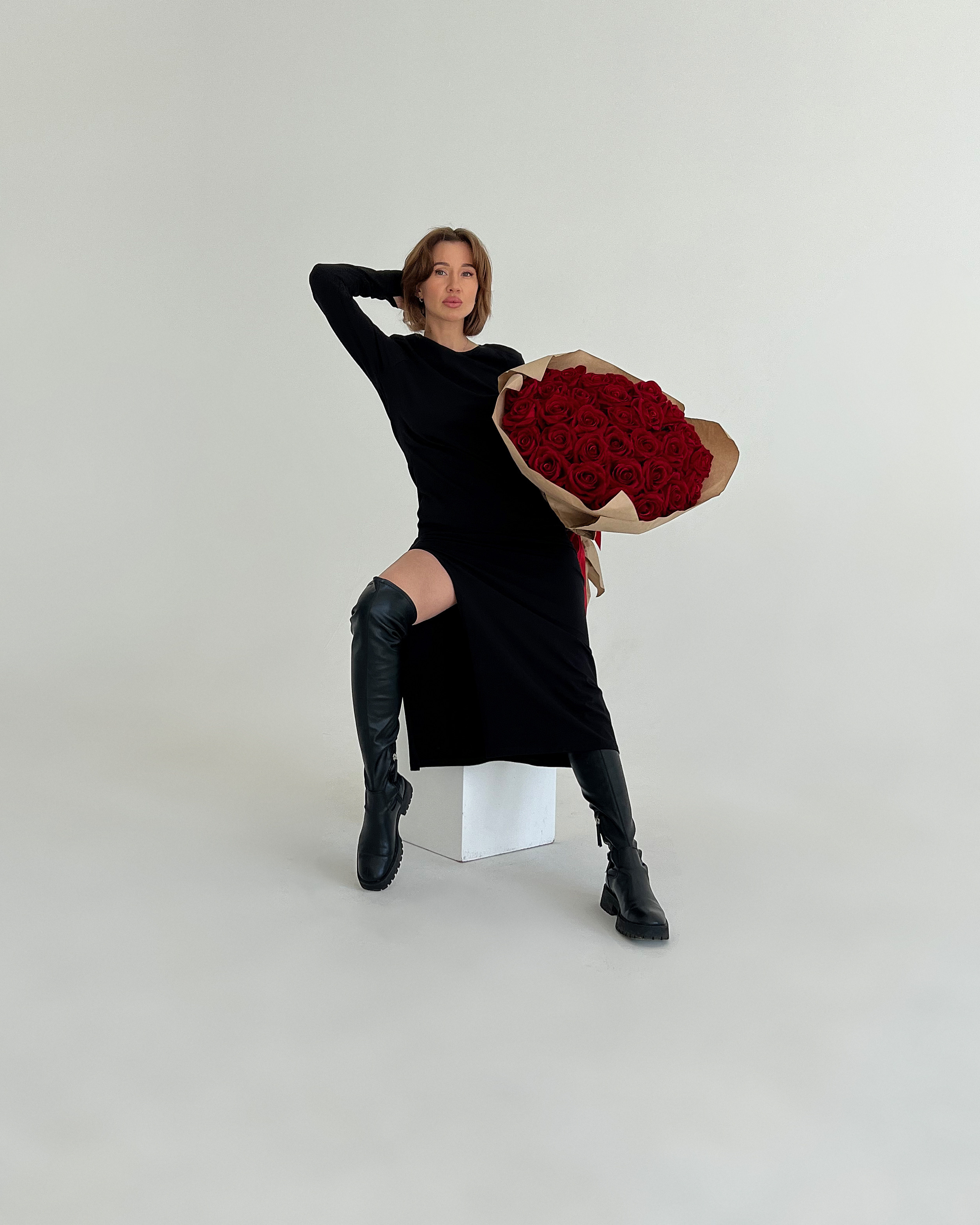 Большой букет красных роз держит красотка в чёрном платье.