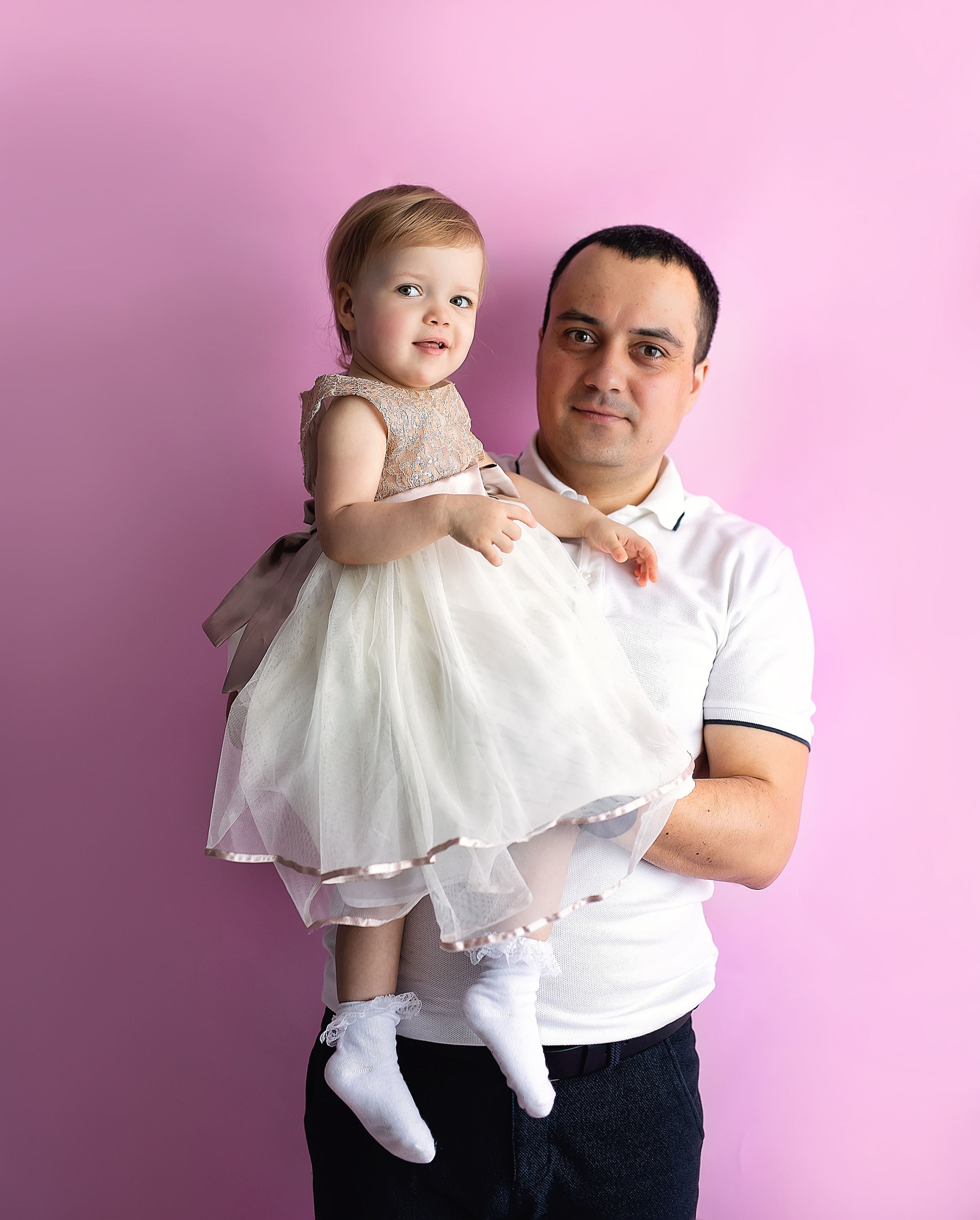 Отец держит свою принцессу на руках на розовом фоне.
