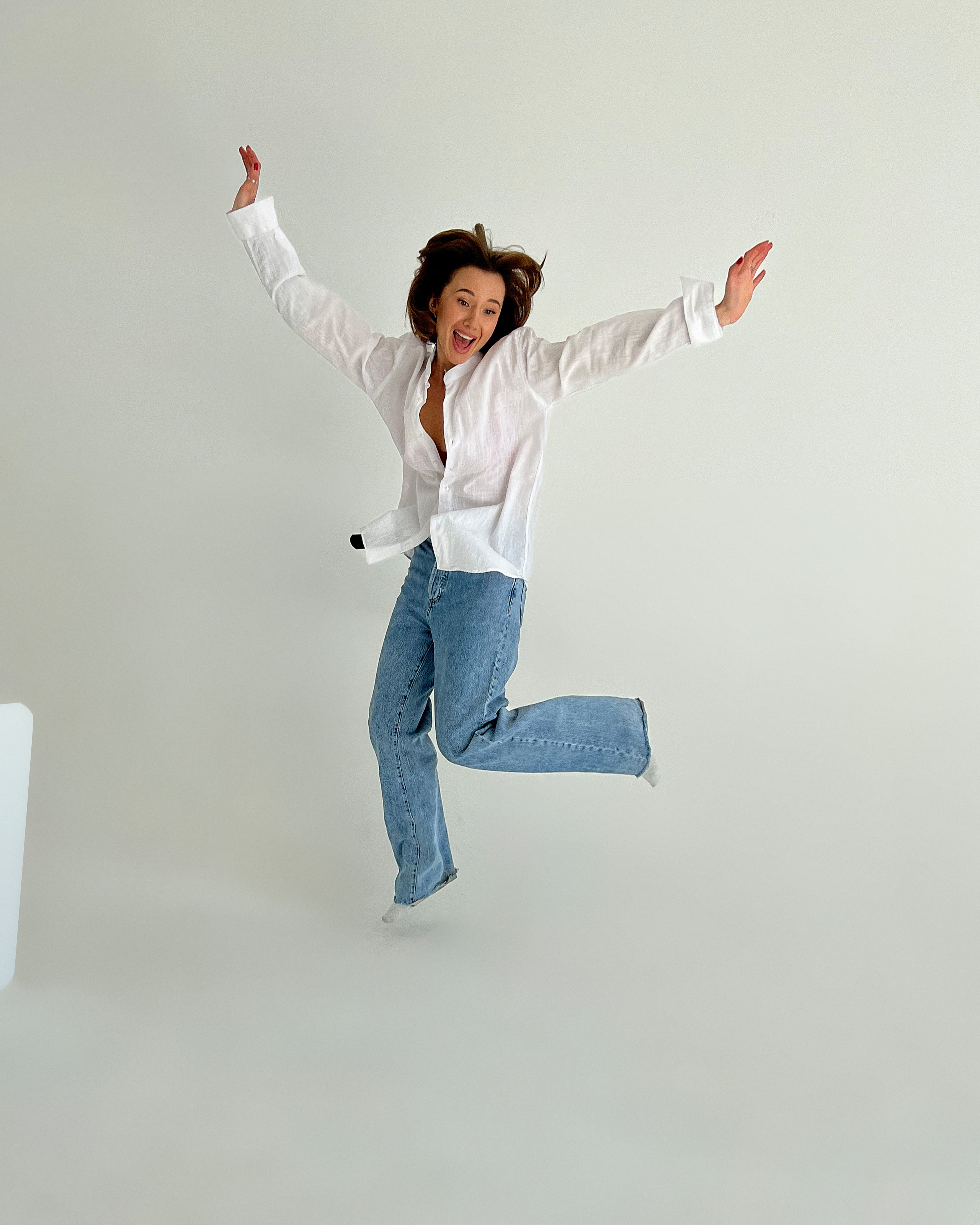 Девушка подпрыгивает воздух на белом фоне её волосы летят наверх.