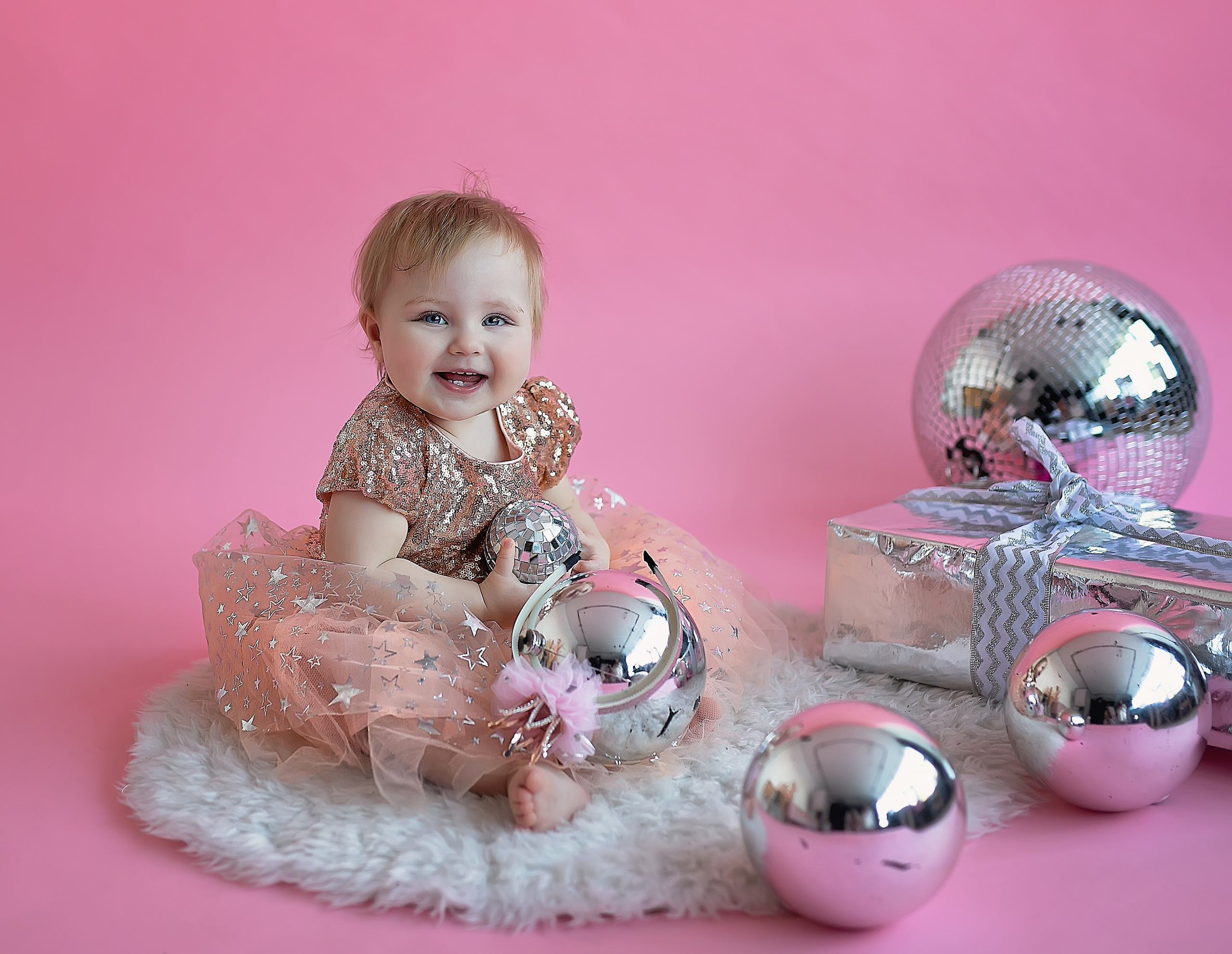 Малышка сидит на полу и смеётся ей очень нравятся зеркальные шары.