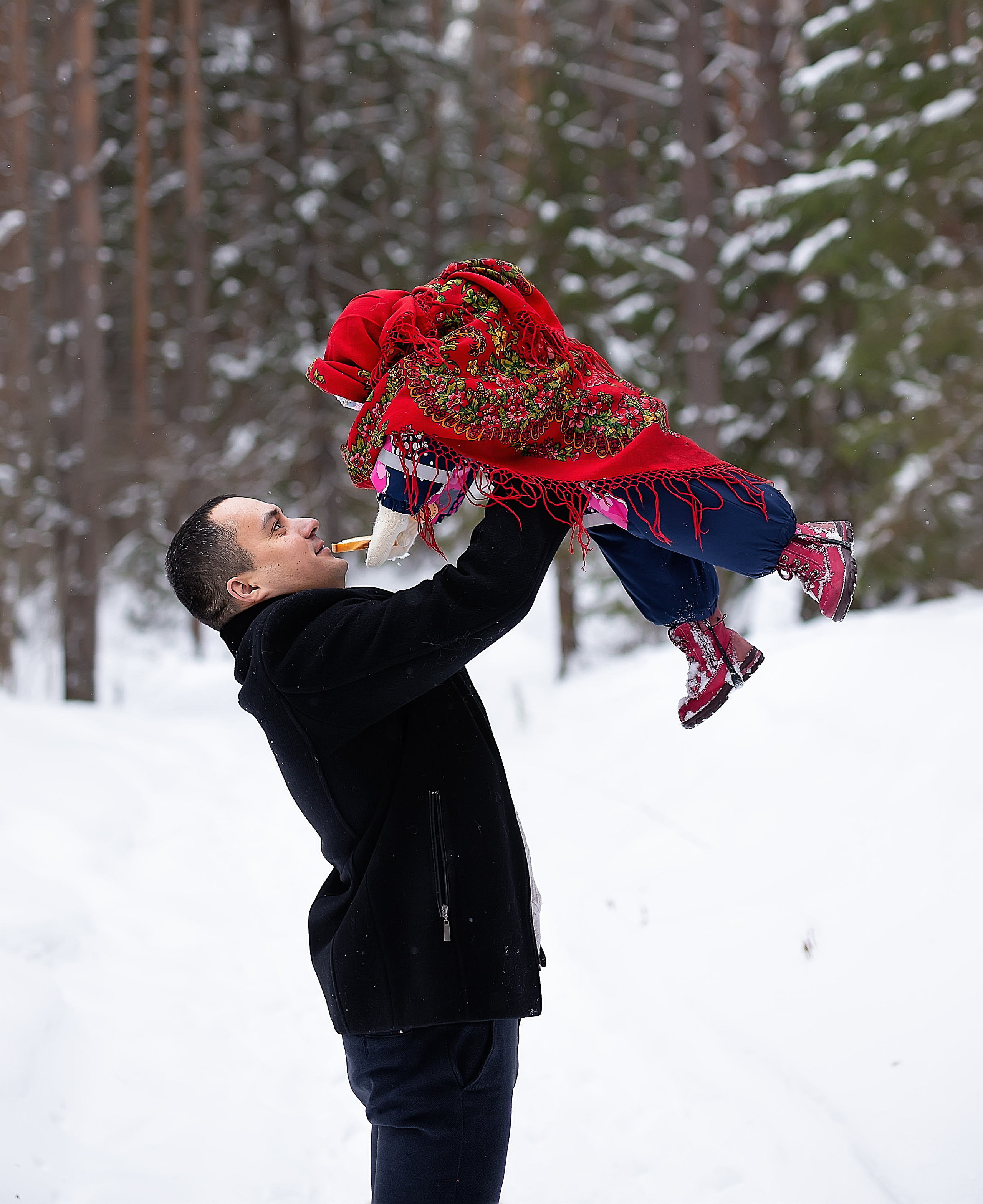 Папа в пальто подкидывает своего ребёнка и любуется на него.