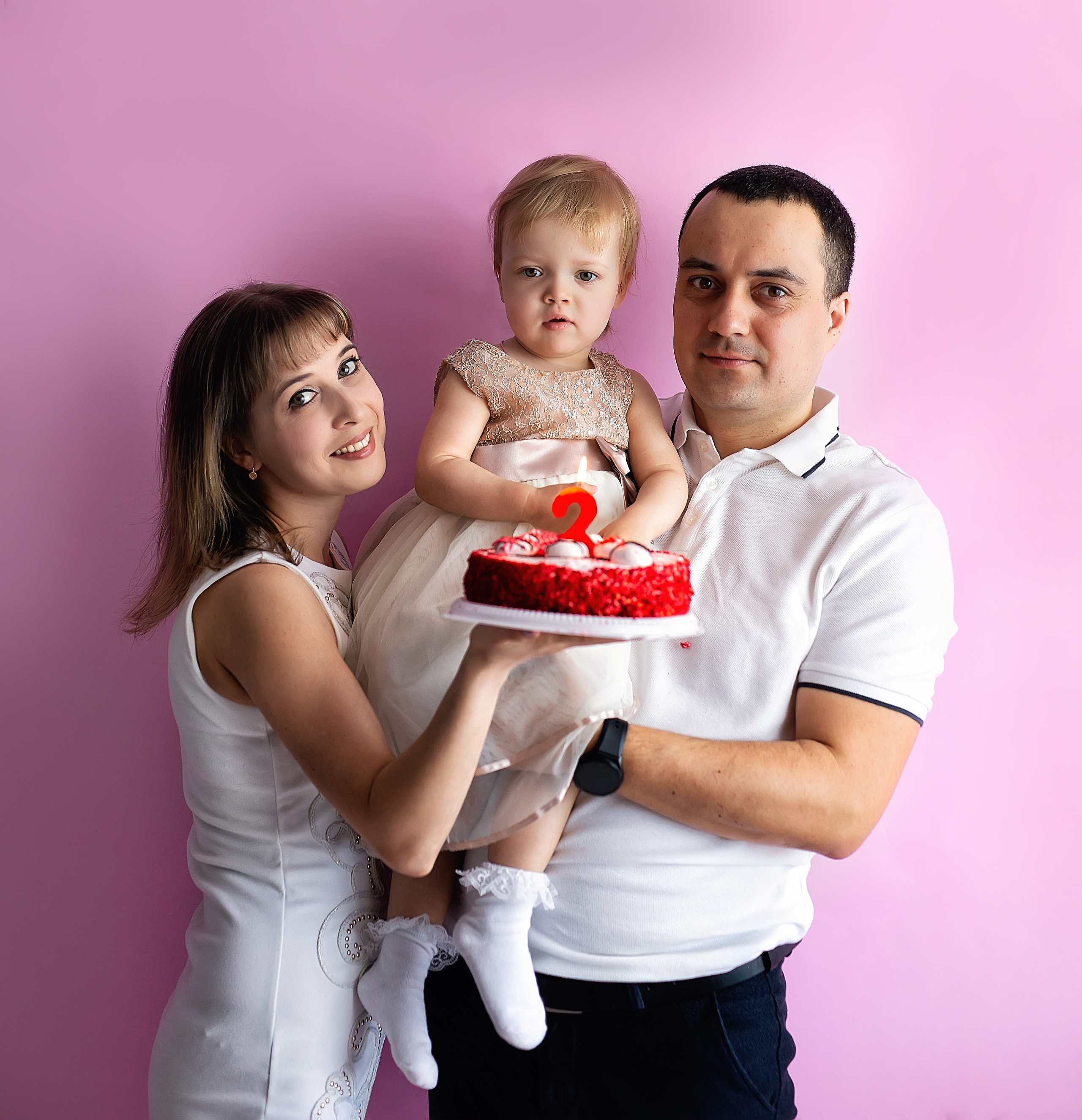 Мама и папа держат дочку на руках в её день рождения.