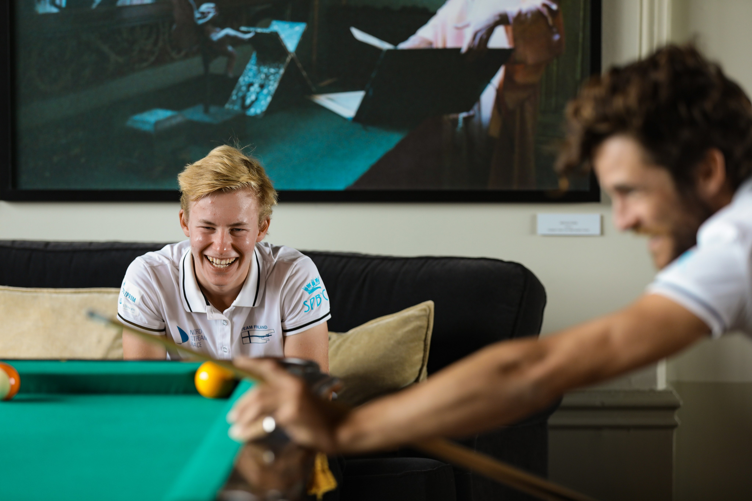 Яхтсмены играют в бильярд во время перерыва между гонками. Репортажные портреты с улыбкой на лице.