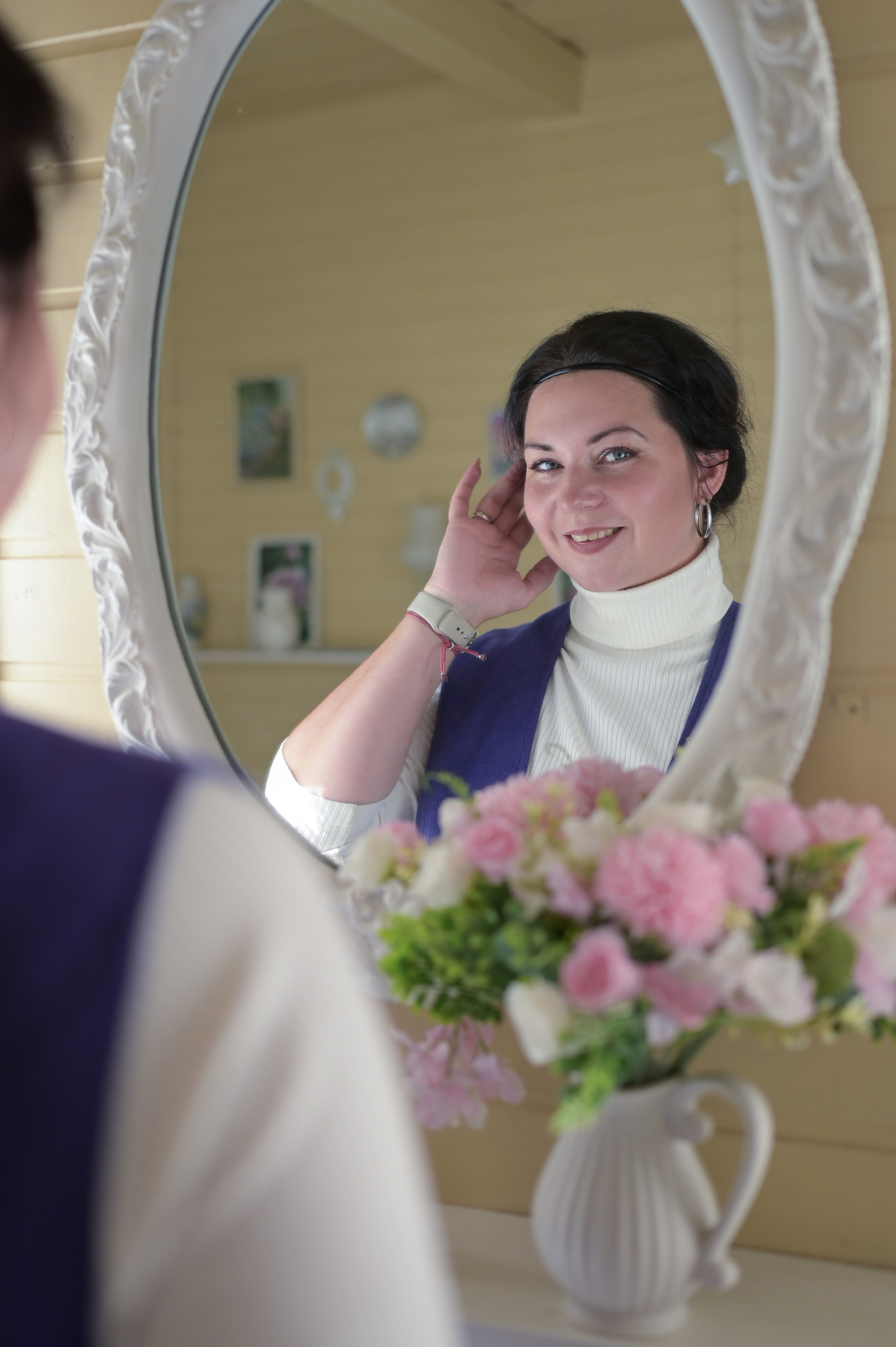 Девушка поправляя прическу кокетливо смотрит на нас через зеркало