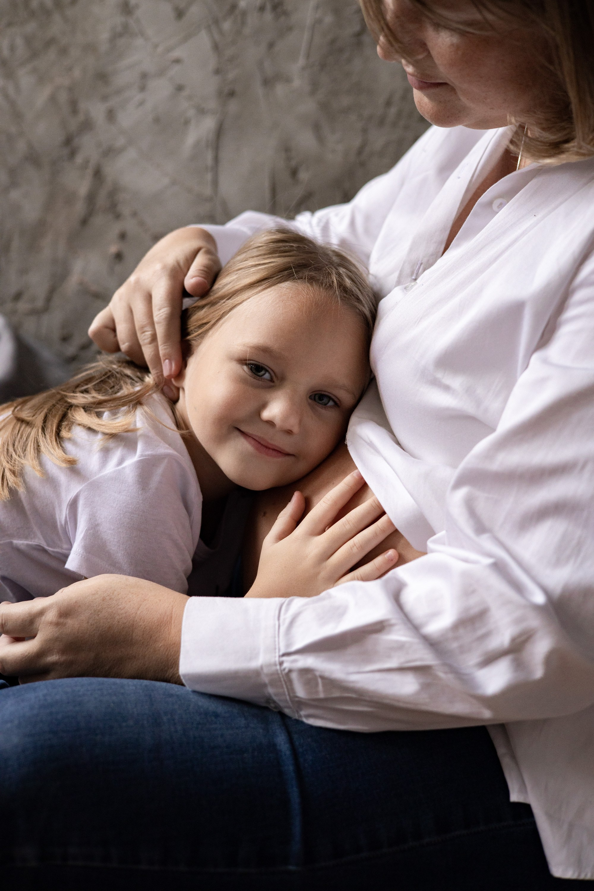 Беременная мама сидит на полу, дочка прислонилась ухом к животу. Фотосессия для беременных  Астрахань.