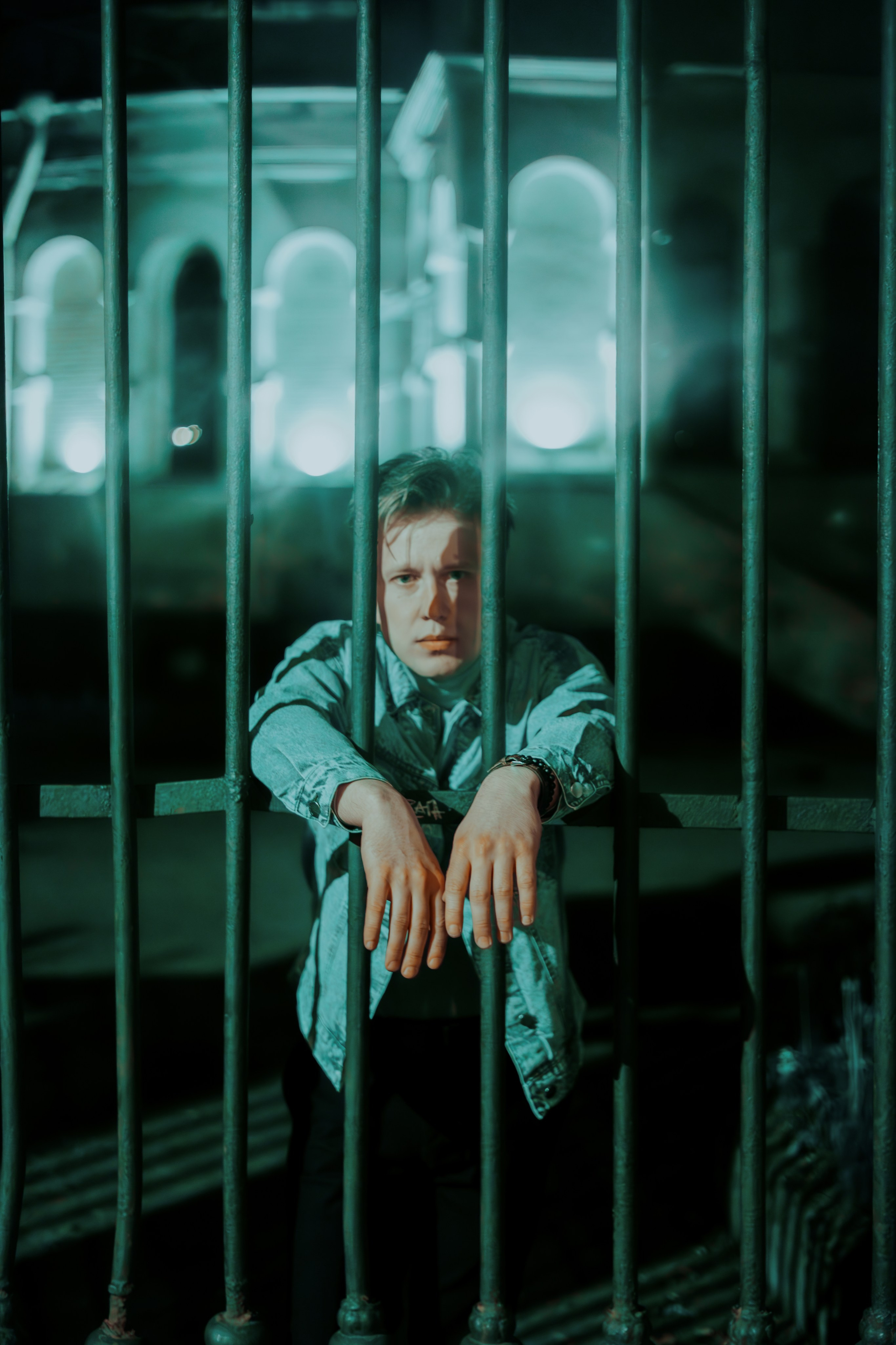 Молодой человек высовывает руки за решетку