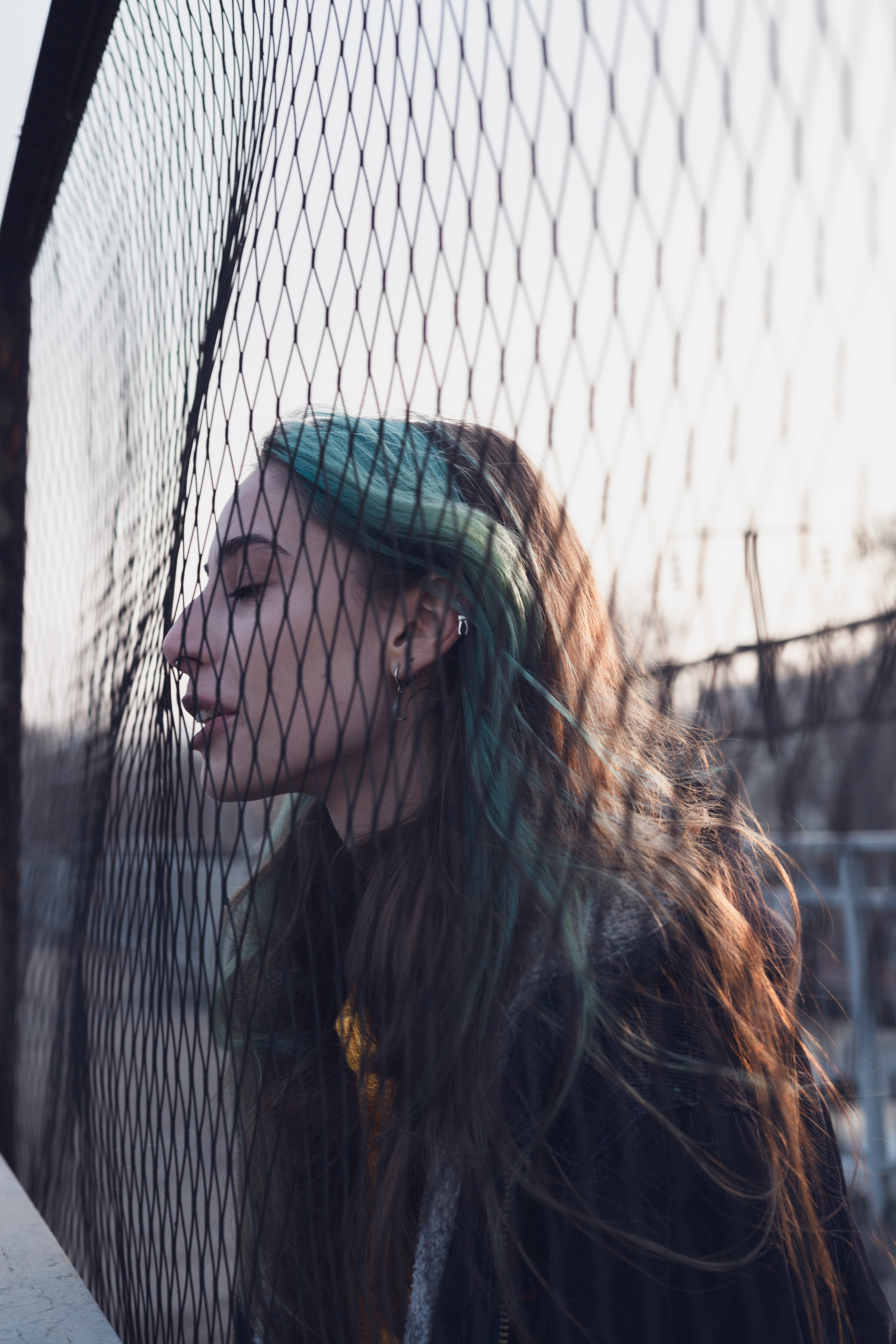 Силуэт девушки у сетки забора на фоне железной дороги