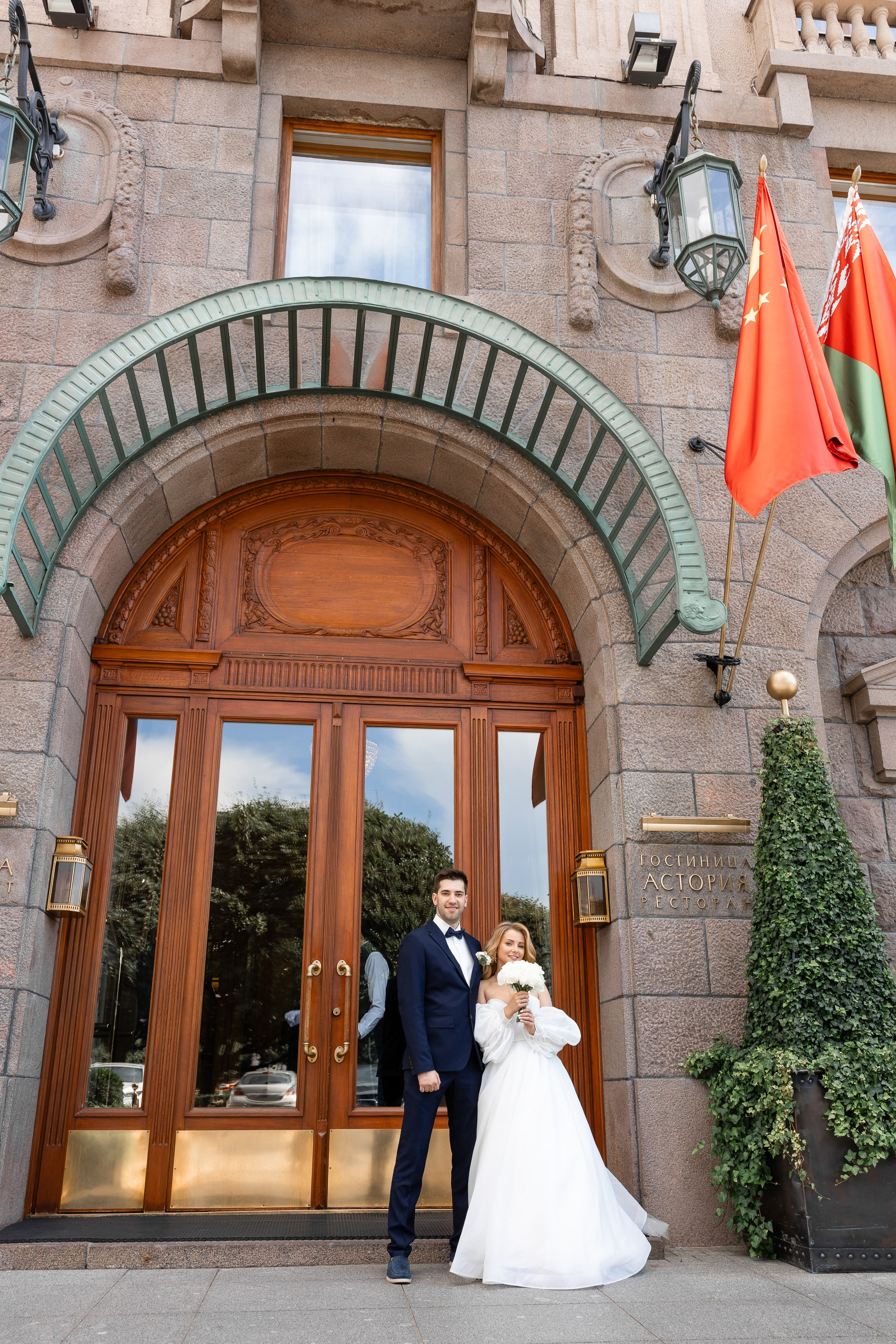Жених и невеста фотографируются на фоне входа в гостиницу Астория