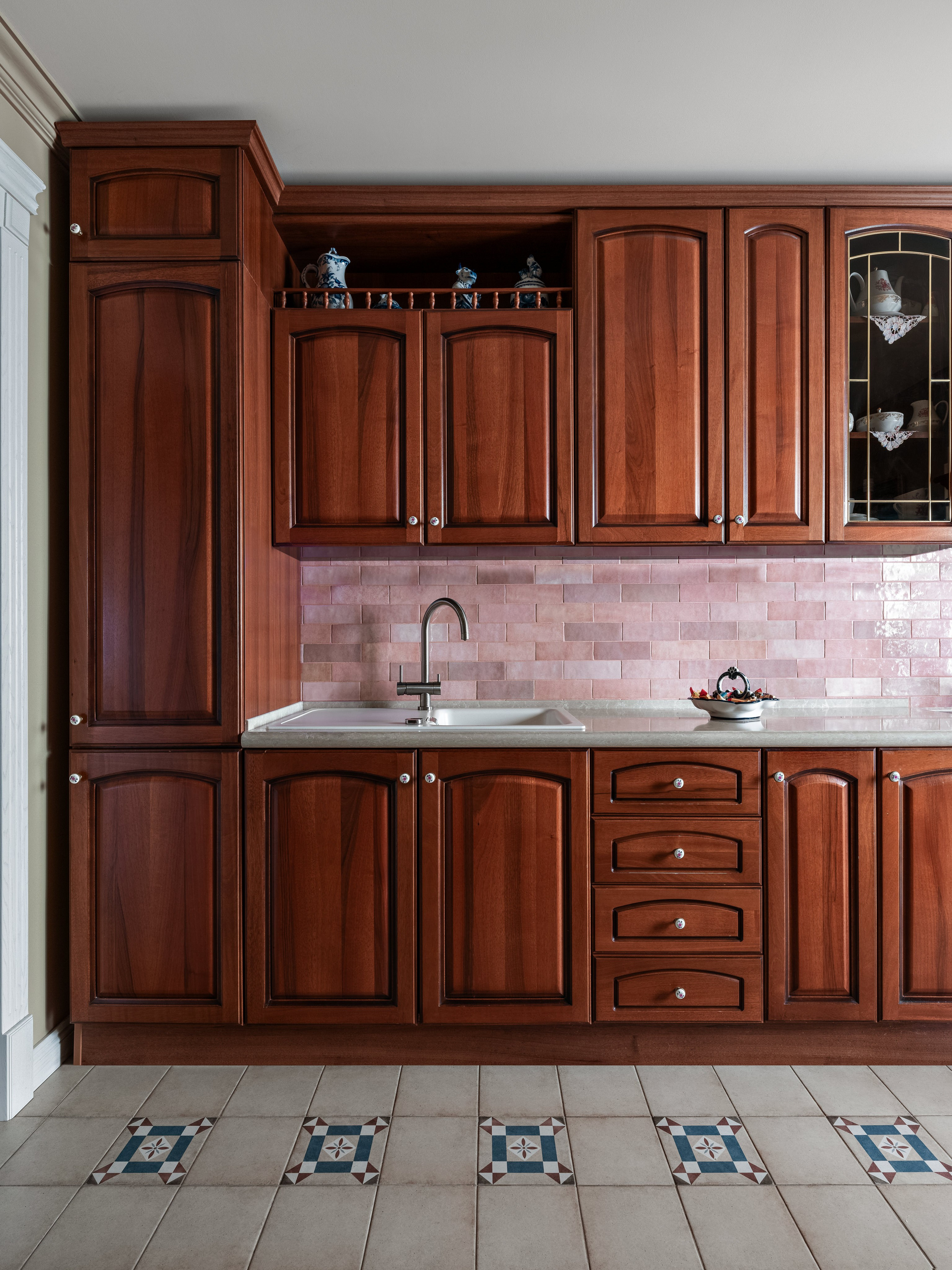 Фото кухни с массивным деревянным гарнитуром, фасадами в классическом стиле и фартуком из плитки нежного розового оттенка. Интерьер сочетает уют и функциональность. Проект Юлии Капункиной и Альбины Терещенко, стилист Алина Нелень, фотограф Сергей Денисенко.