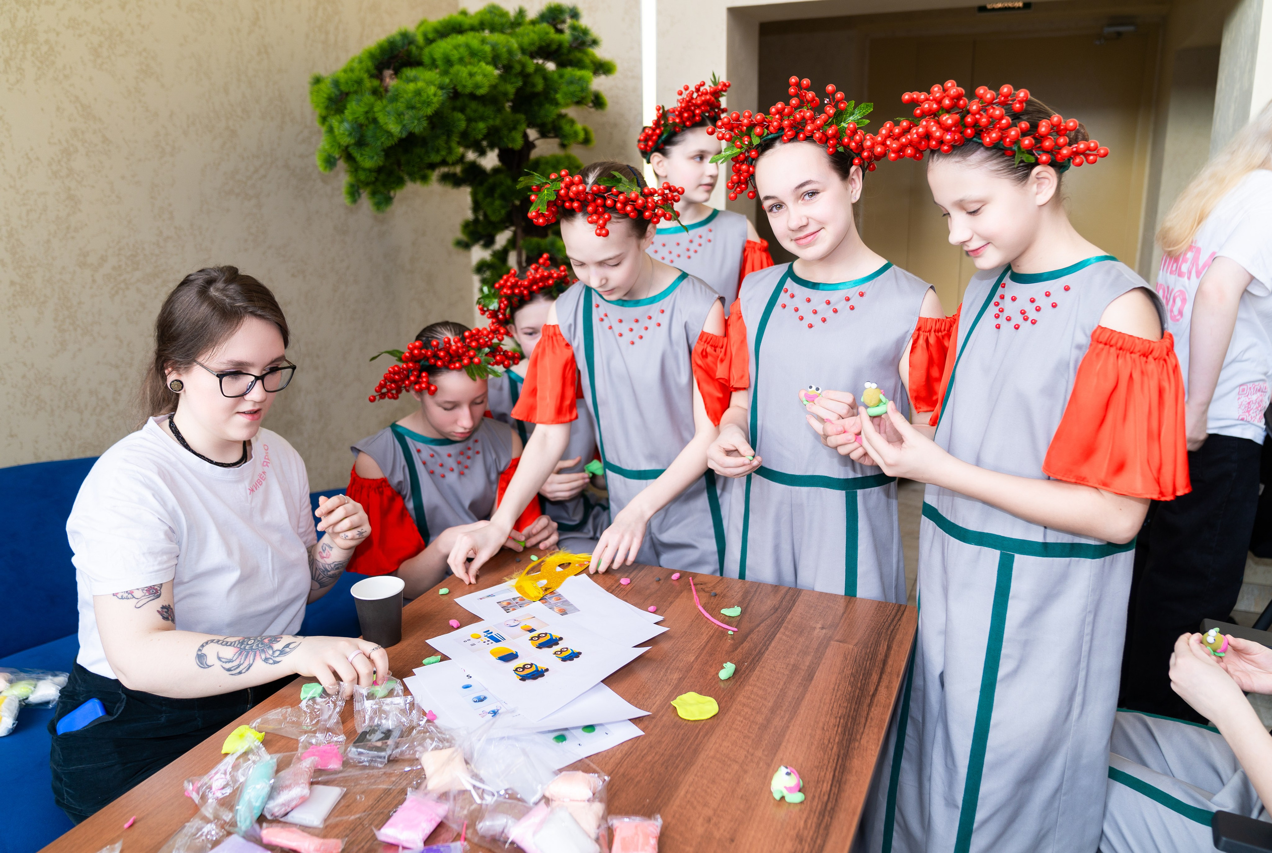 Девочки в серых платьях с красными венками из рябины мастерят поделки за столом на инклюзивном балу «Мы все равны». Фотограф Мальцев Евгений.