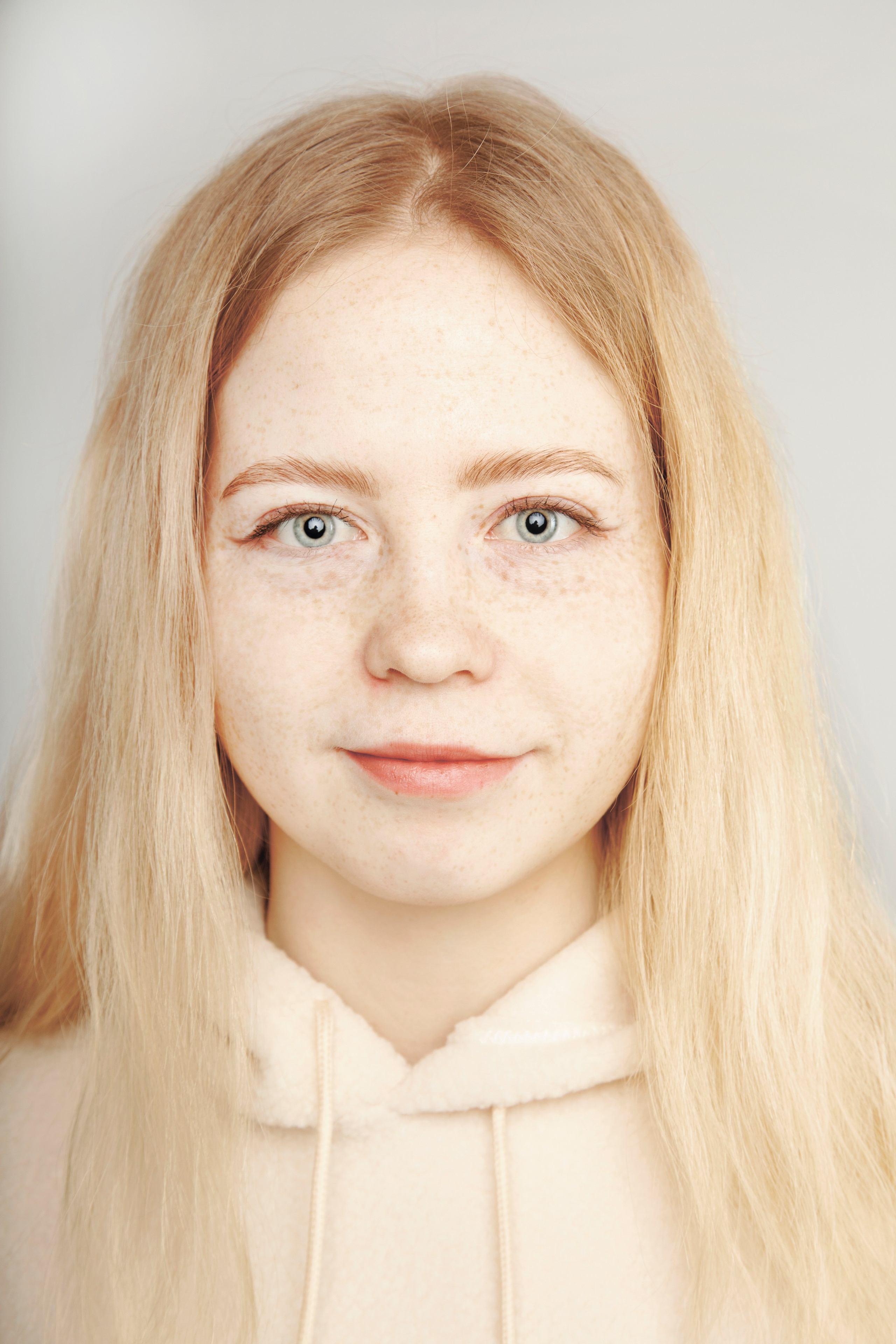 Портрет светловолосой и голубоглазой девушки с веснушками. В светлой одежде на белом фоне.