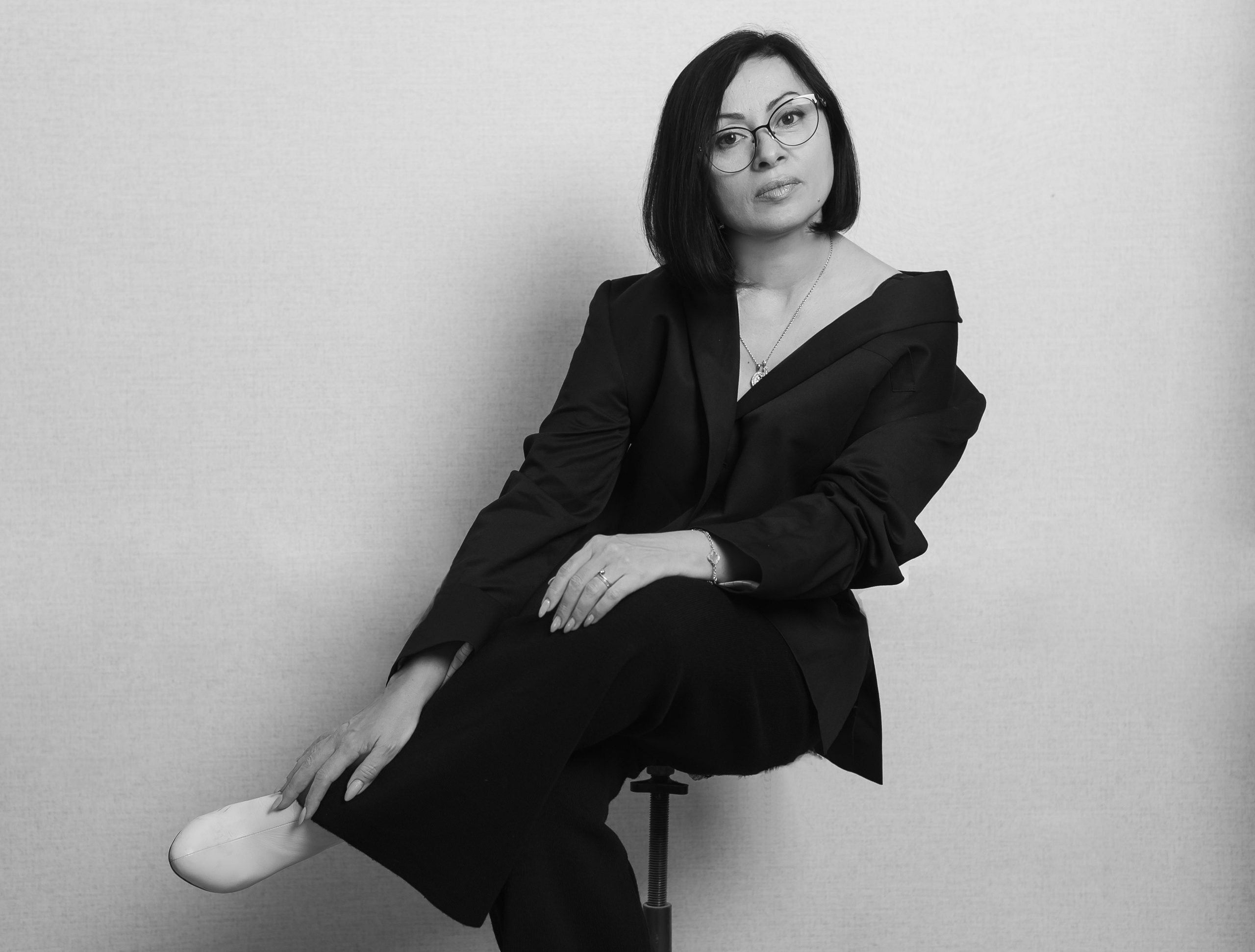 Девушка в черном пиджаке красиво сидит на стуле.