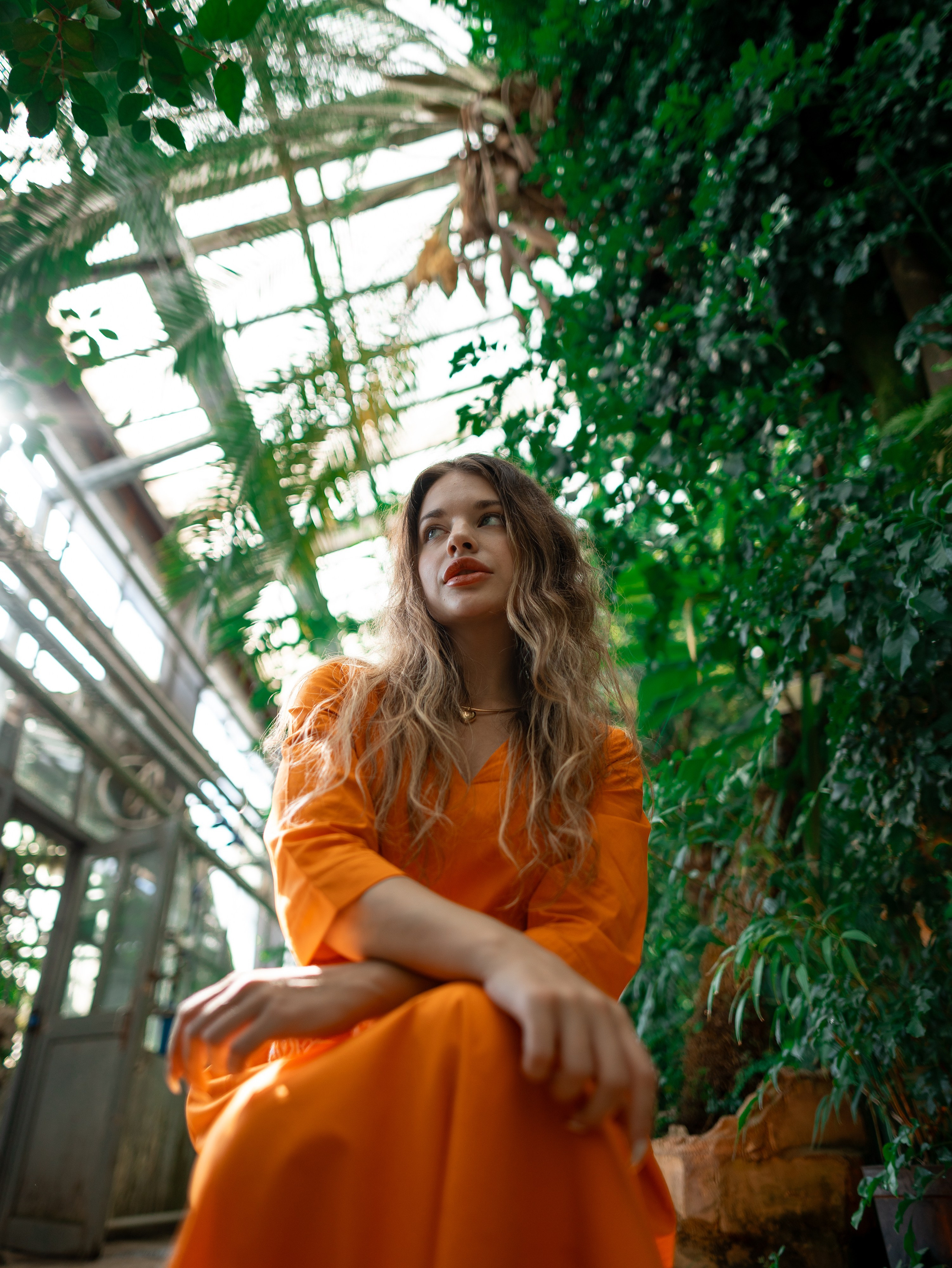 Девушка в оранжевом платье стоит на фоне зелени