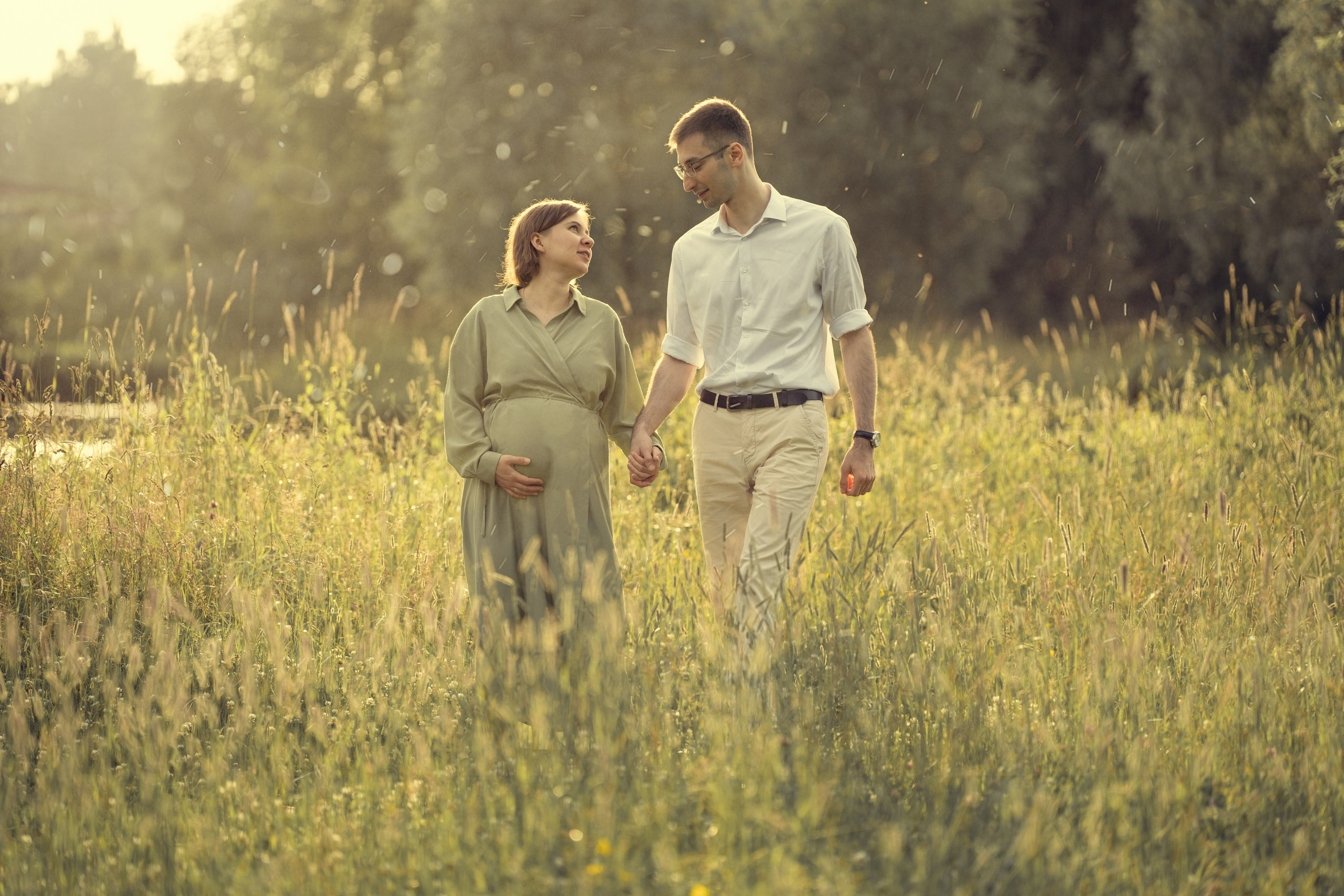 Беременная девушка с мужем прогуливаются летом в парке.