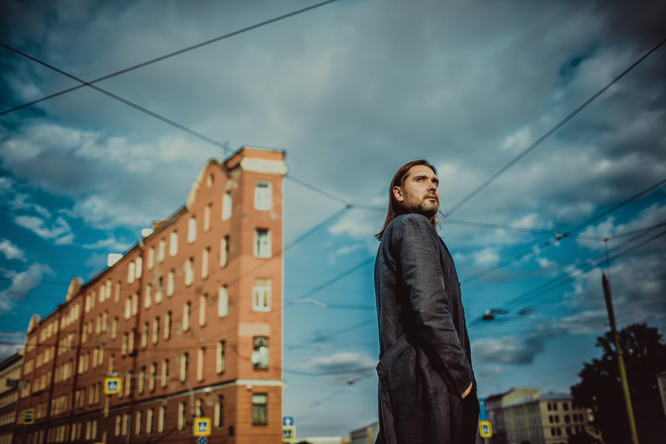 стильный парень в пальто на фоне линий трамвайных проводов