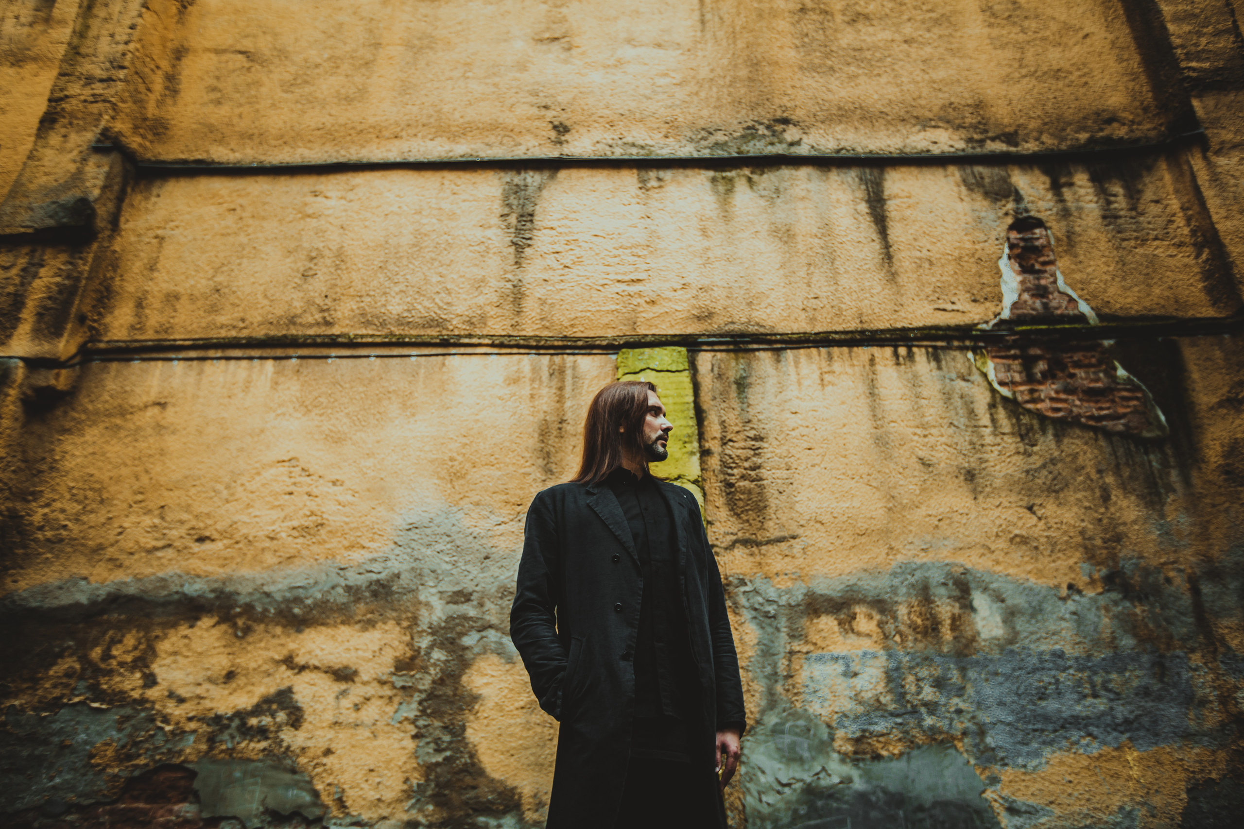 мужчина в черном одеянии стоит в профиль у старой оранжевой стены