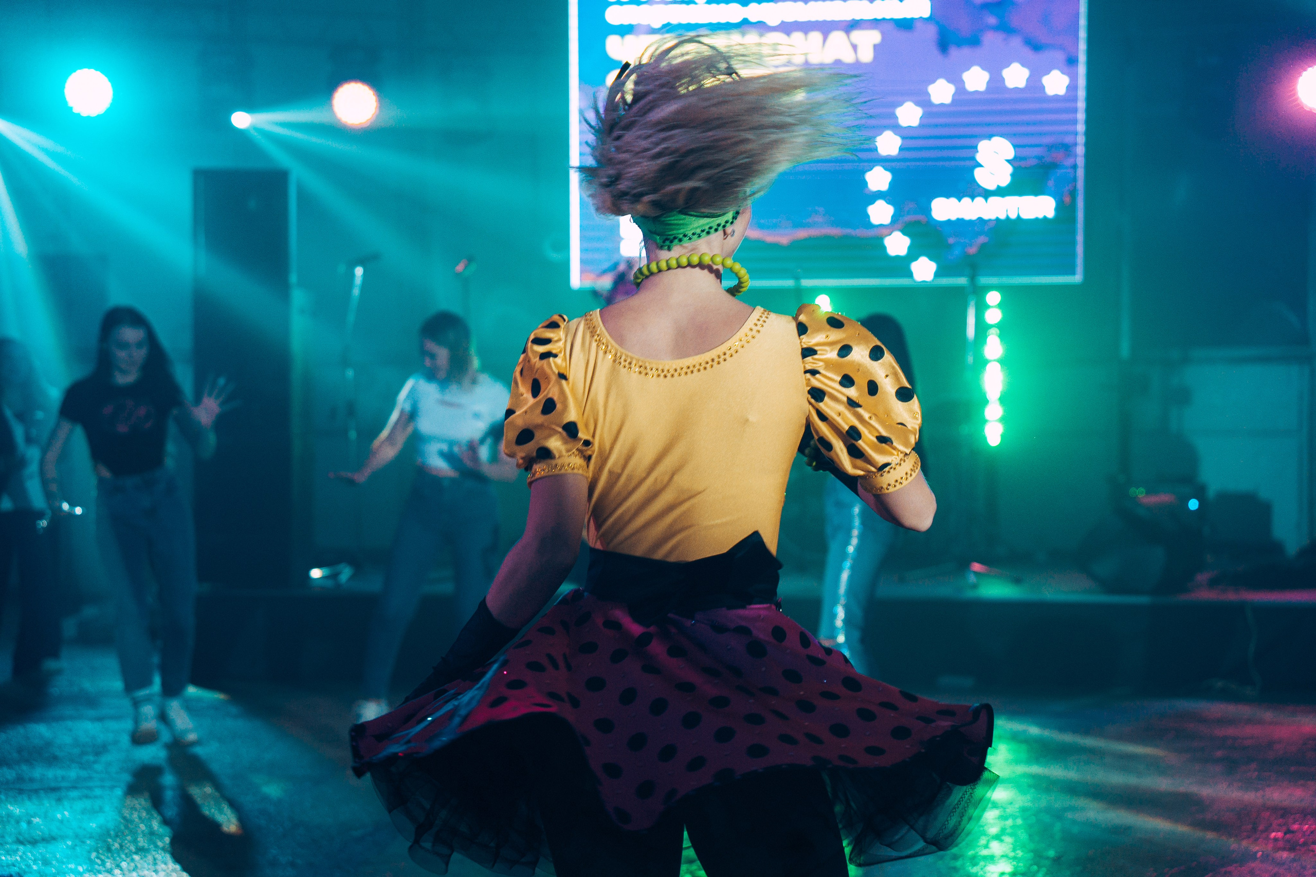 Девушка в эффектном золотом костюме выступает на сцене, за ней — профессиональное освещение и экран