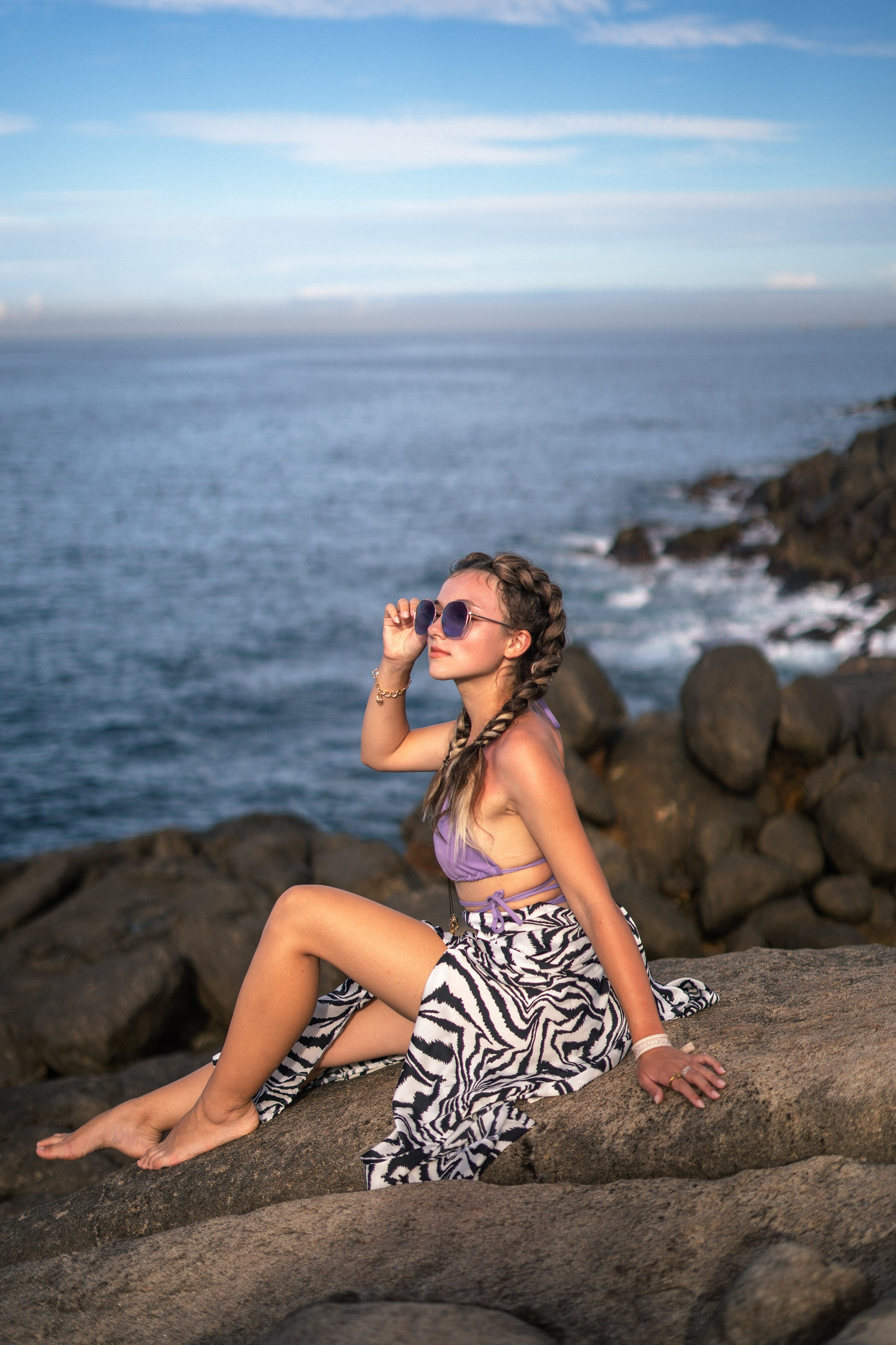 a girl in a purple swimsuit sitting on the rocks with an ocean view