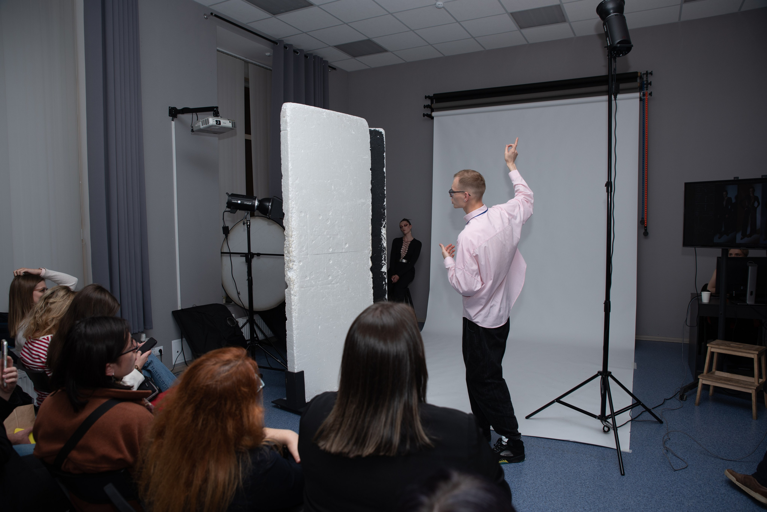 Лекция по фотографии. Фотограф стоит перед слушателями, указывает на источник света.