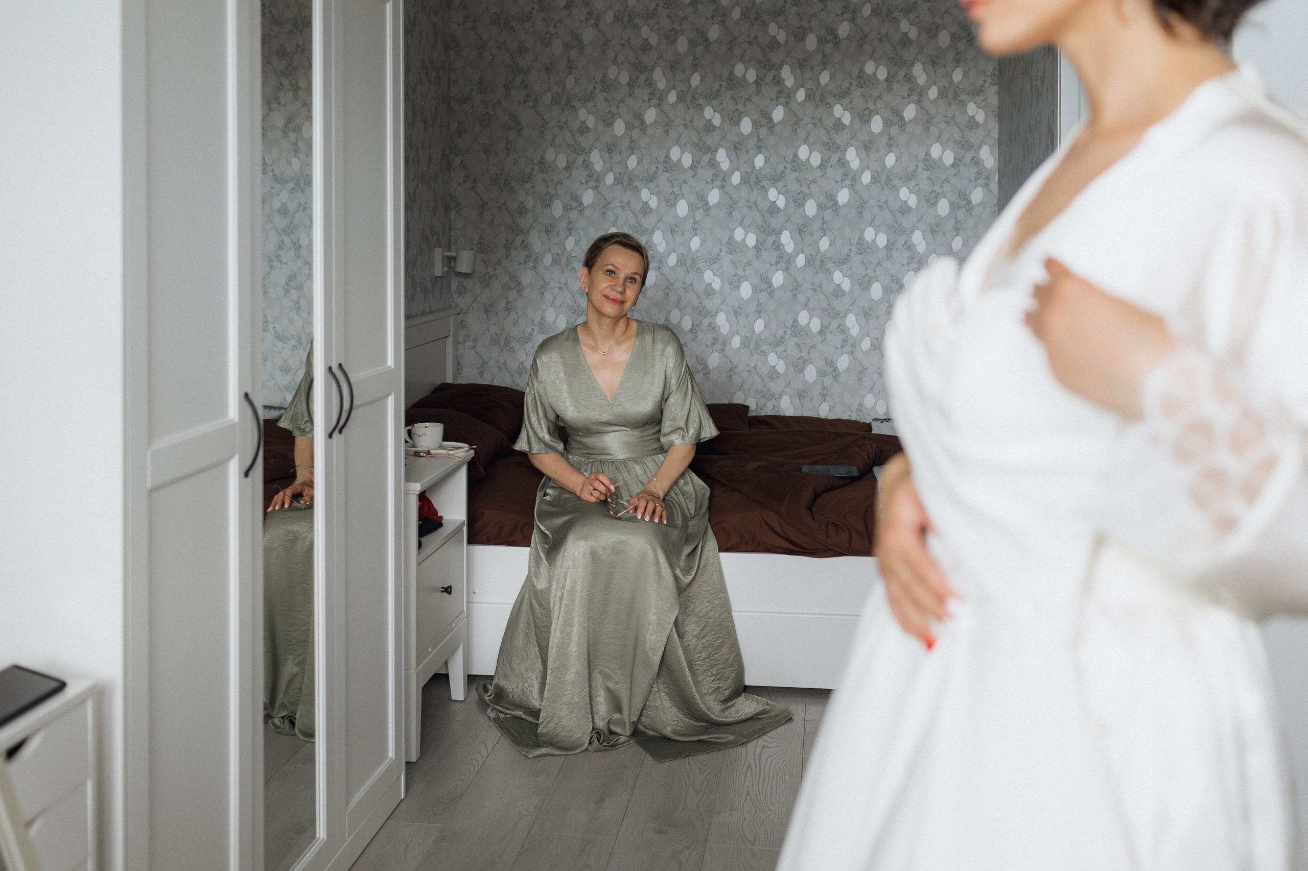 Эмоциональный кадр для свадебного блога: мать запечатлела момент, когда дочь с атласным платьем любуется им перед зеркалом