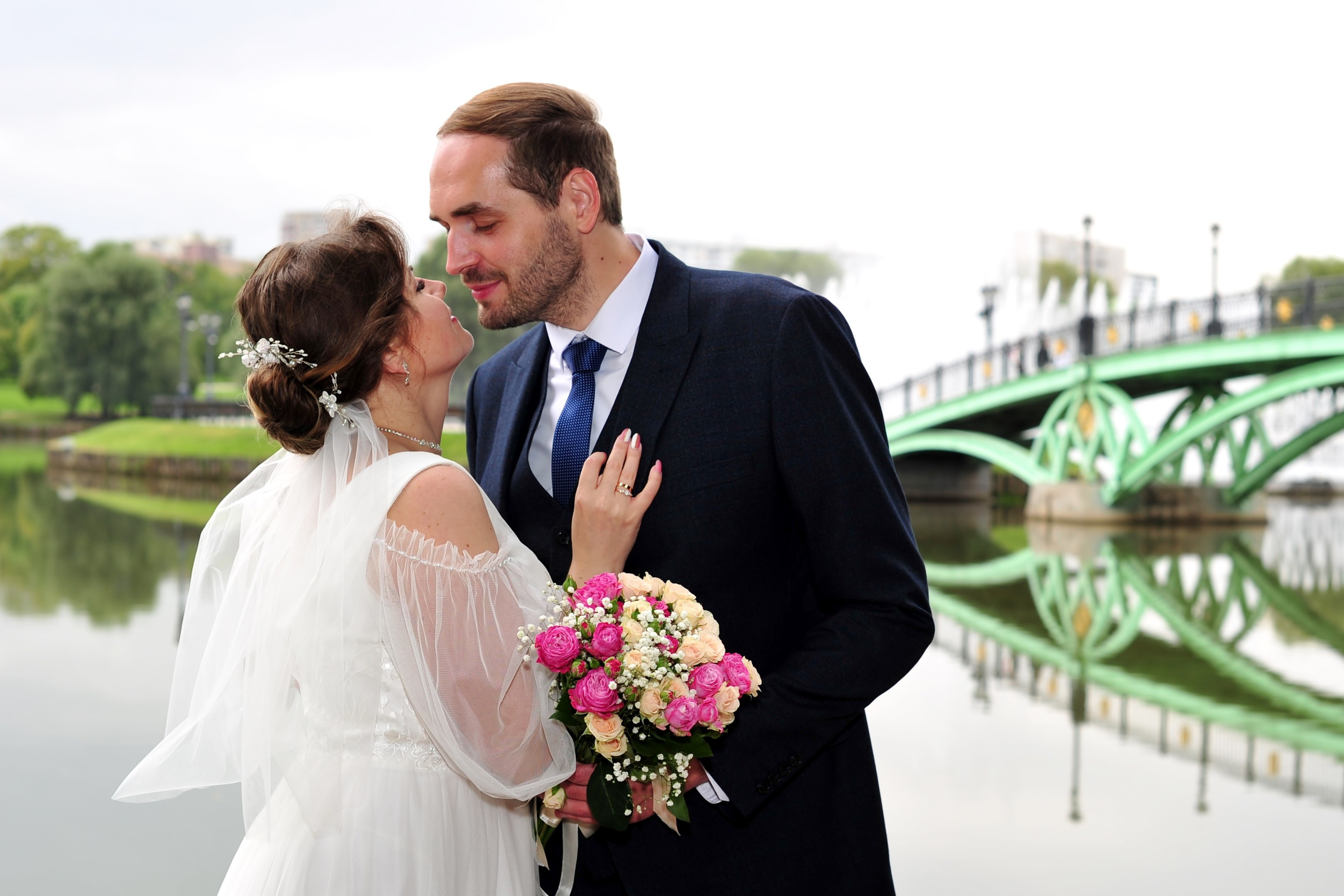 Свадьба в Царицыно пасмурным летним днем, поцелуй новобрачных на фоне металлического моста и пруда 