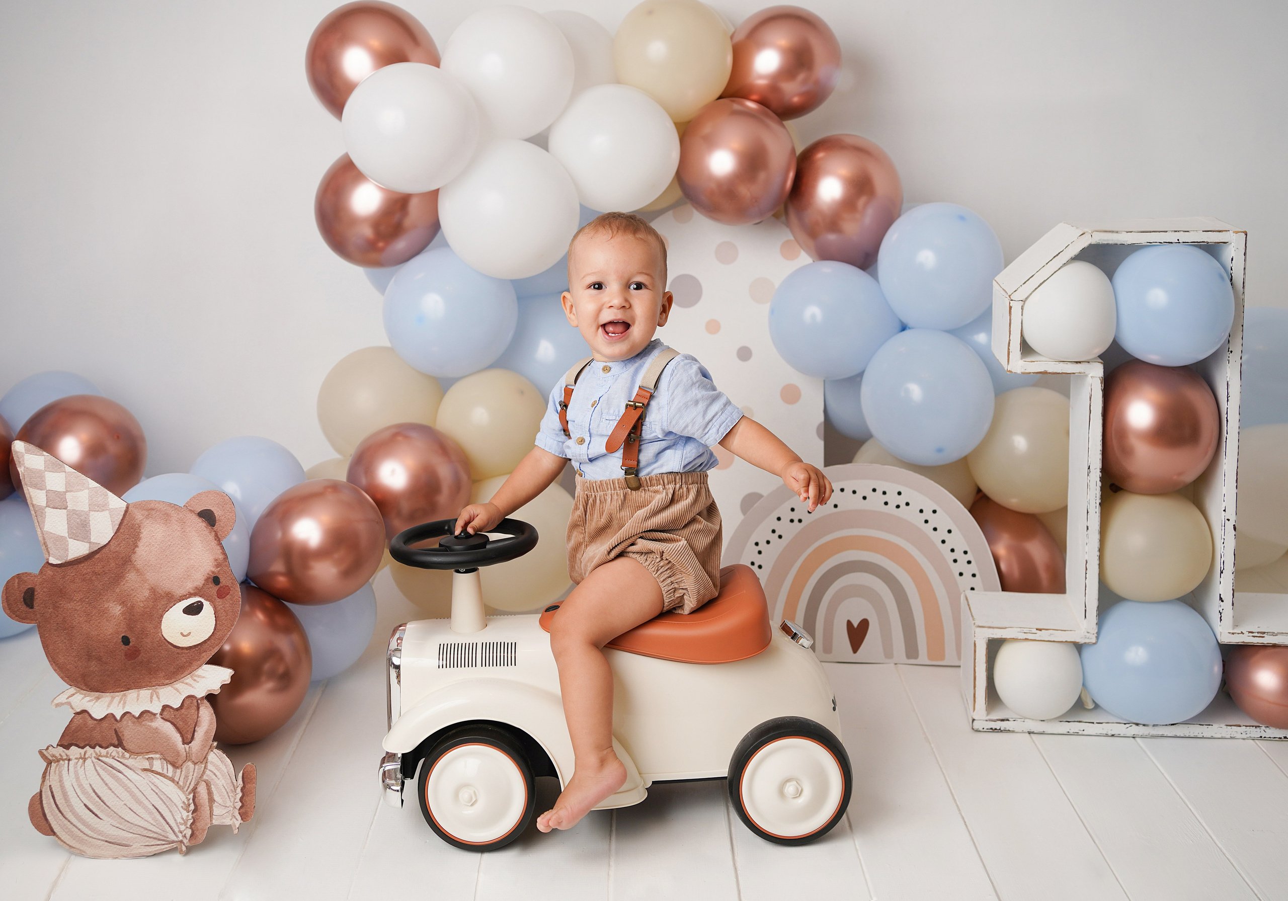 На фото мальчик на фотосессии Первый год. Рядом красивые шарики, Огромная единица, мишка. Малыш едет на машинке.