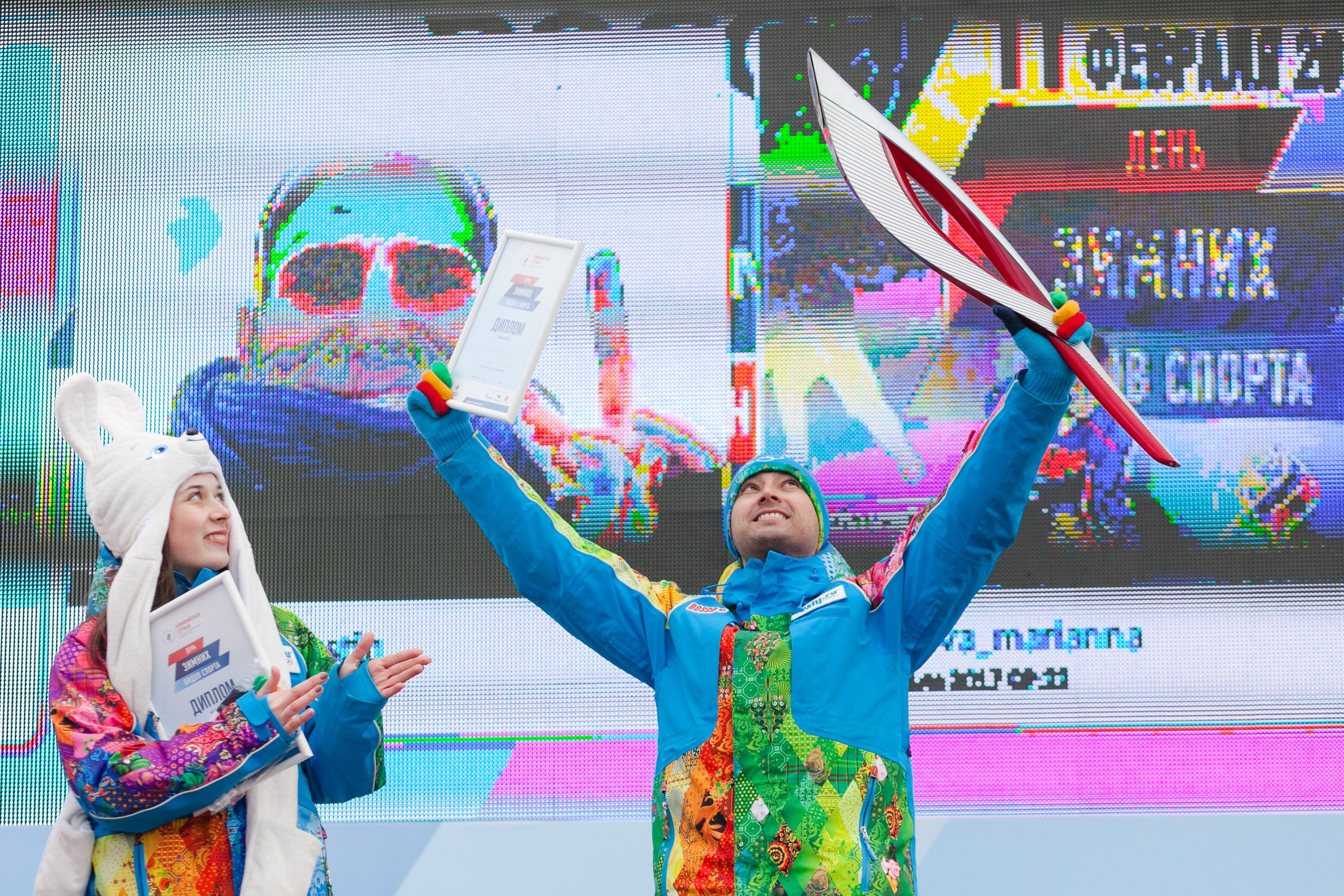 Парень на фестивале зимних видов спорта держит руках олимпийский факел