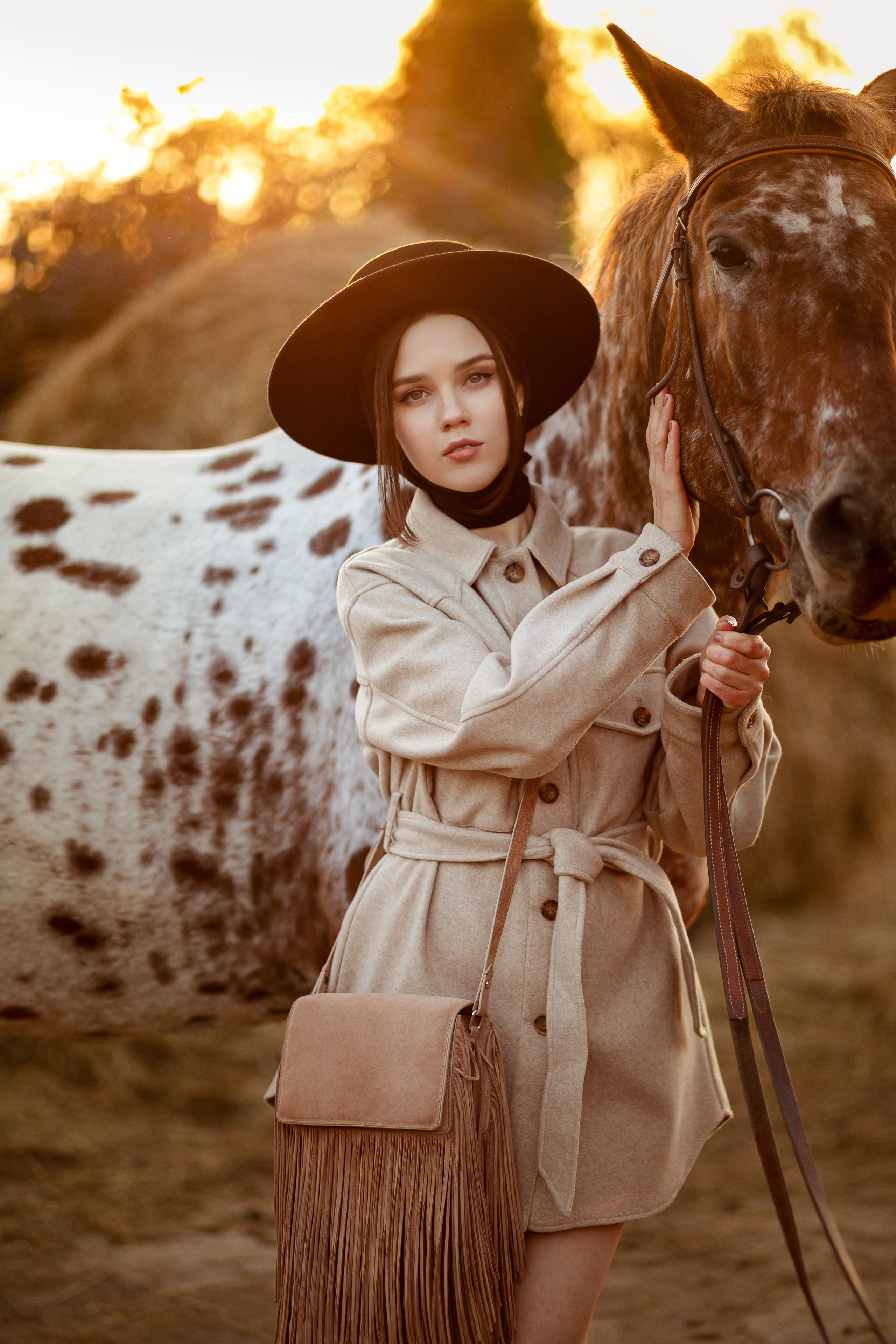 Девушка держит лошадь за шею, на фоне заходящего солнца