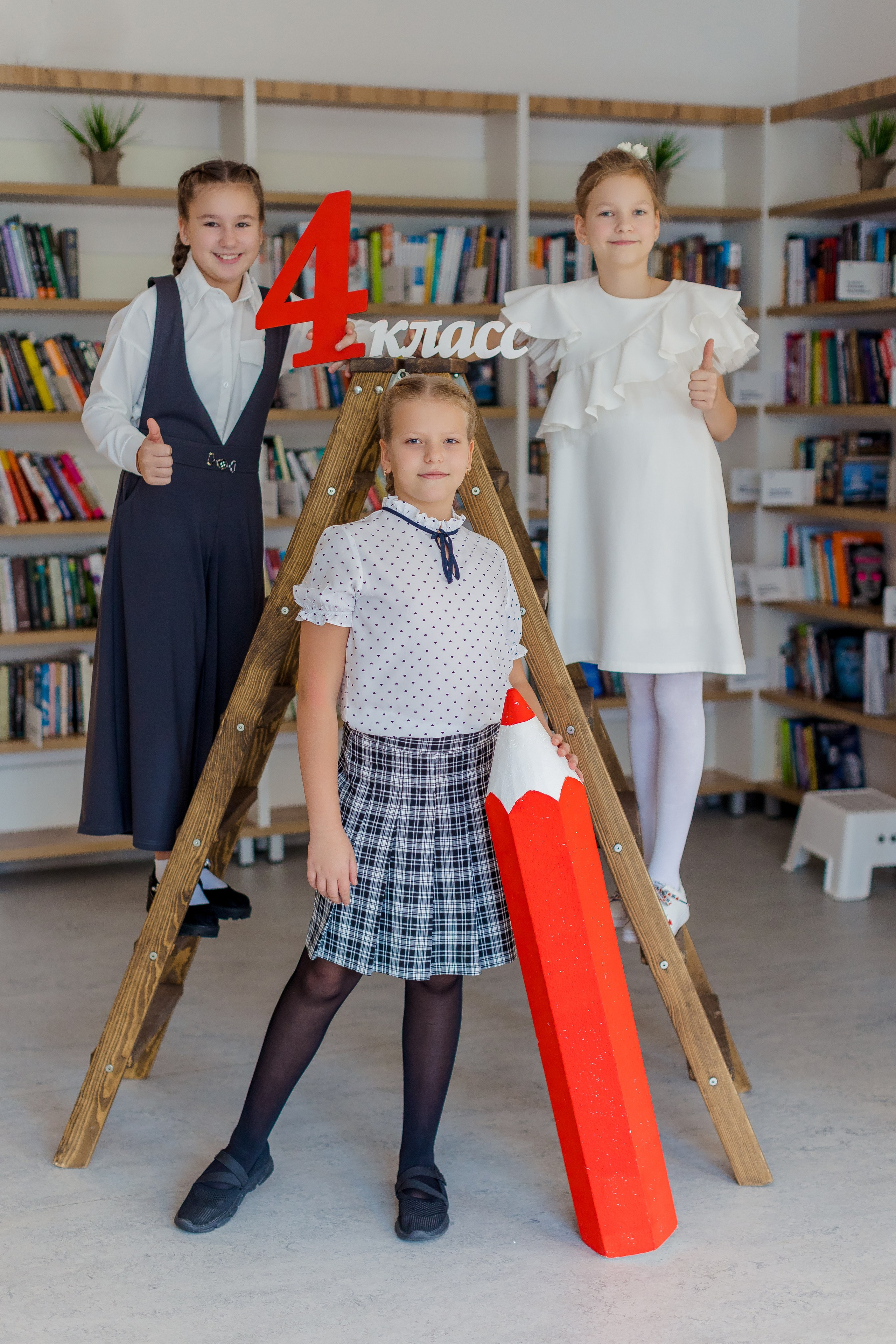 Девочки стоят на лестнице с карандашом и надписью 4 класс в библиотеке