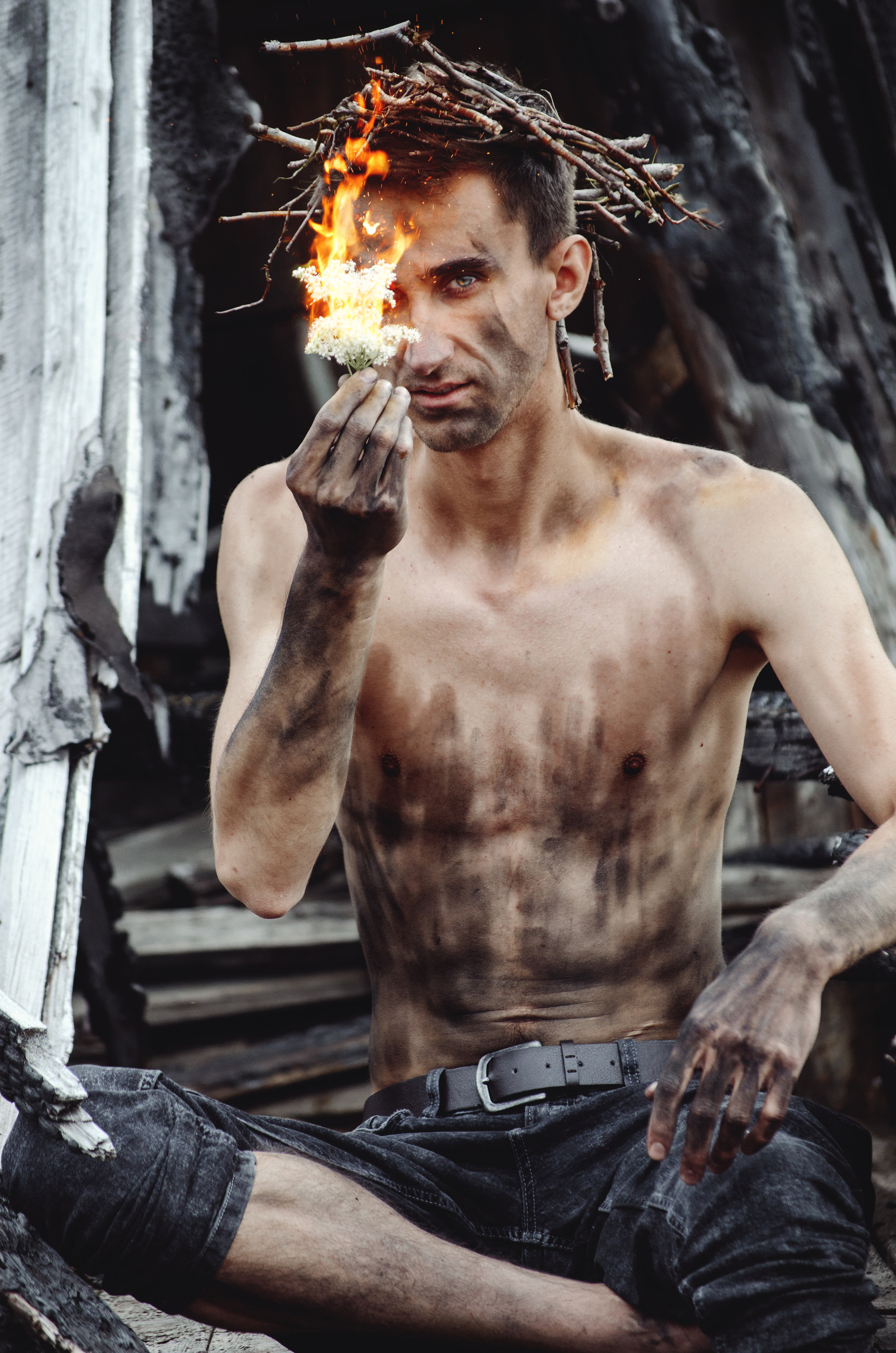 Парень сидит на руинах обгорелого дома, а в руке - огонь