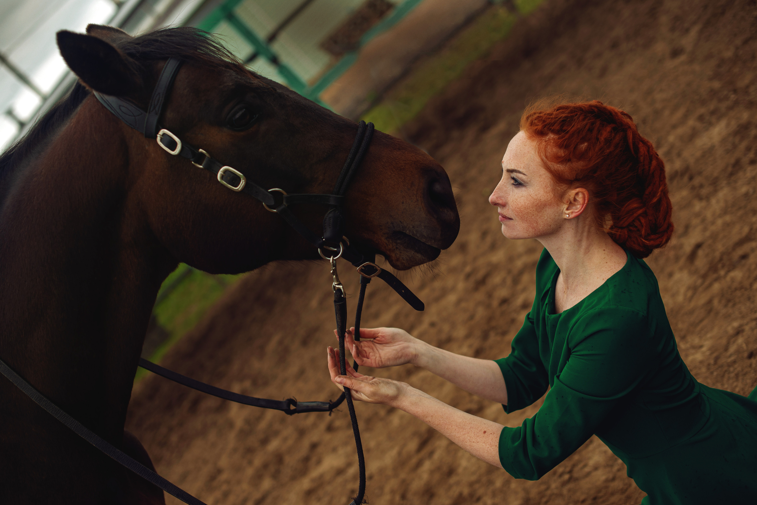 Девушка в зеленом платье смотрит в глаза лошади