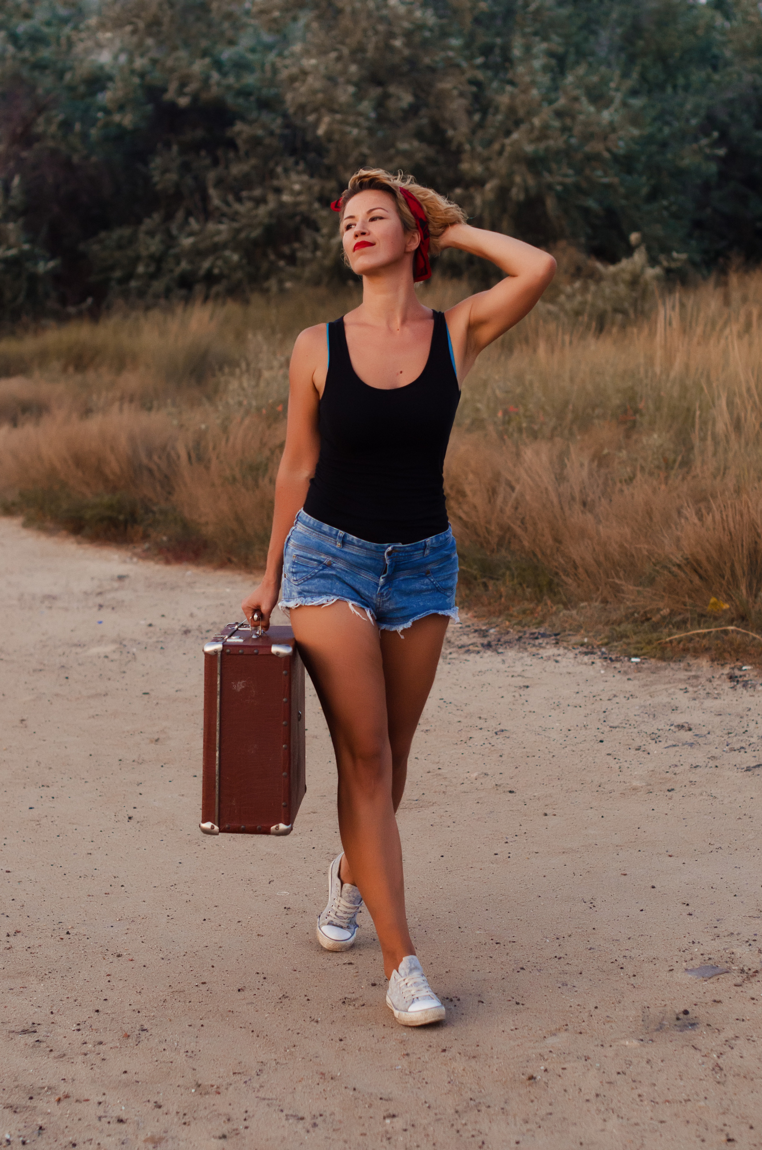 Девушка в шортах идет по дороге с чемоданом