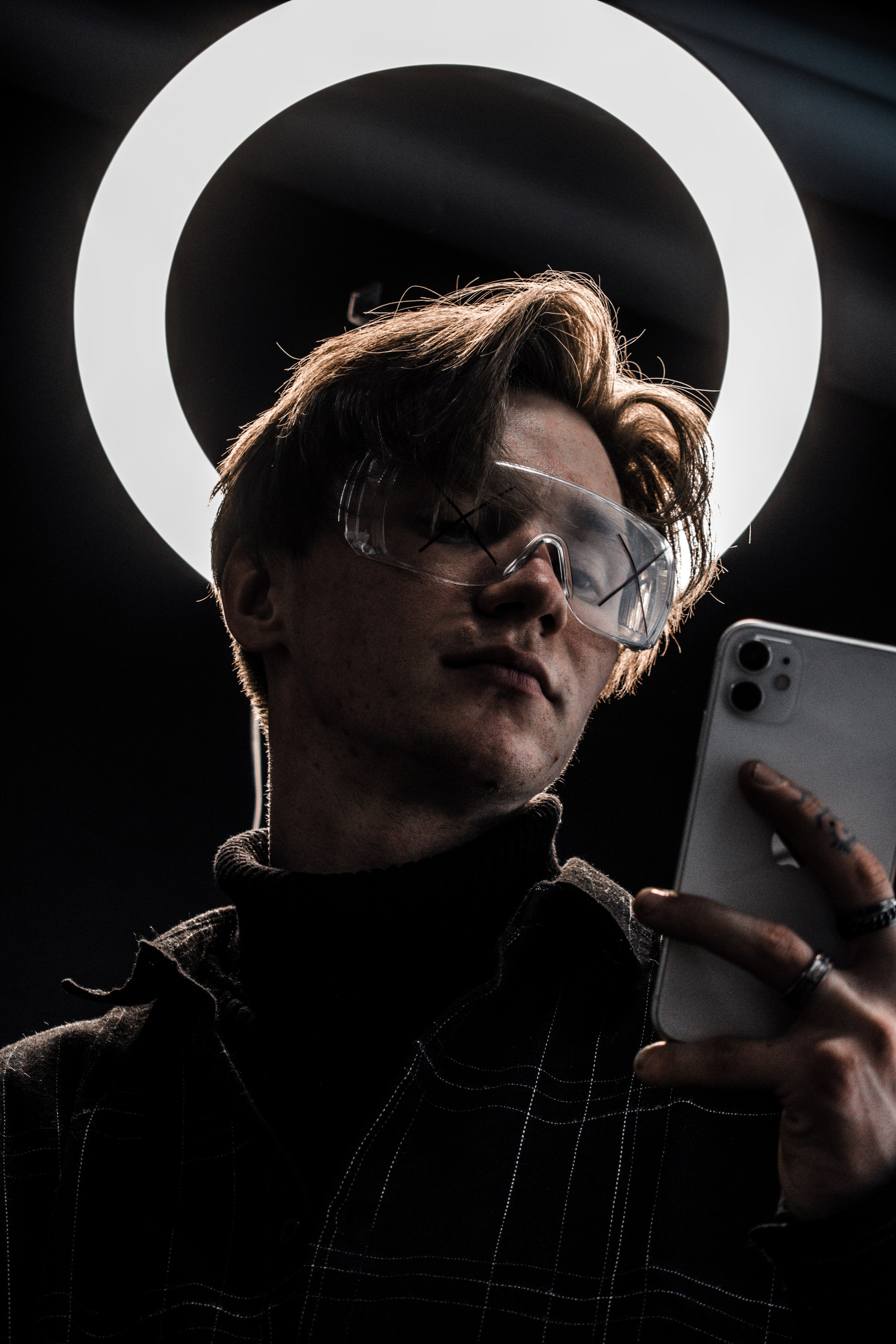 парень смотрит в телефон на фоне кольцевой лампы напоминающей нимб