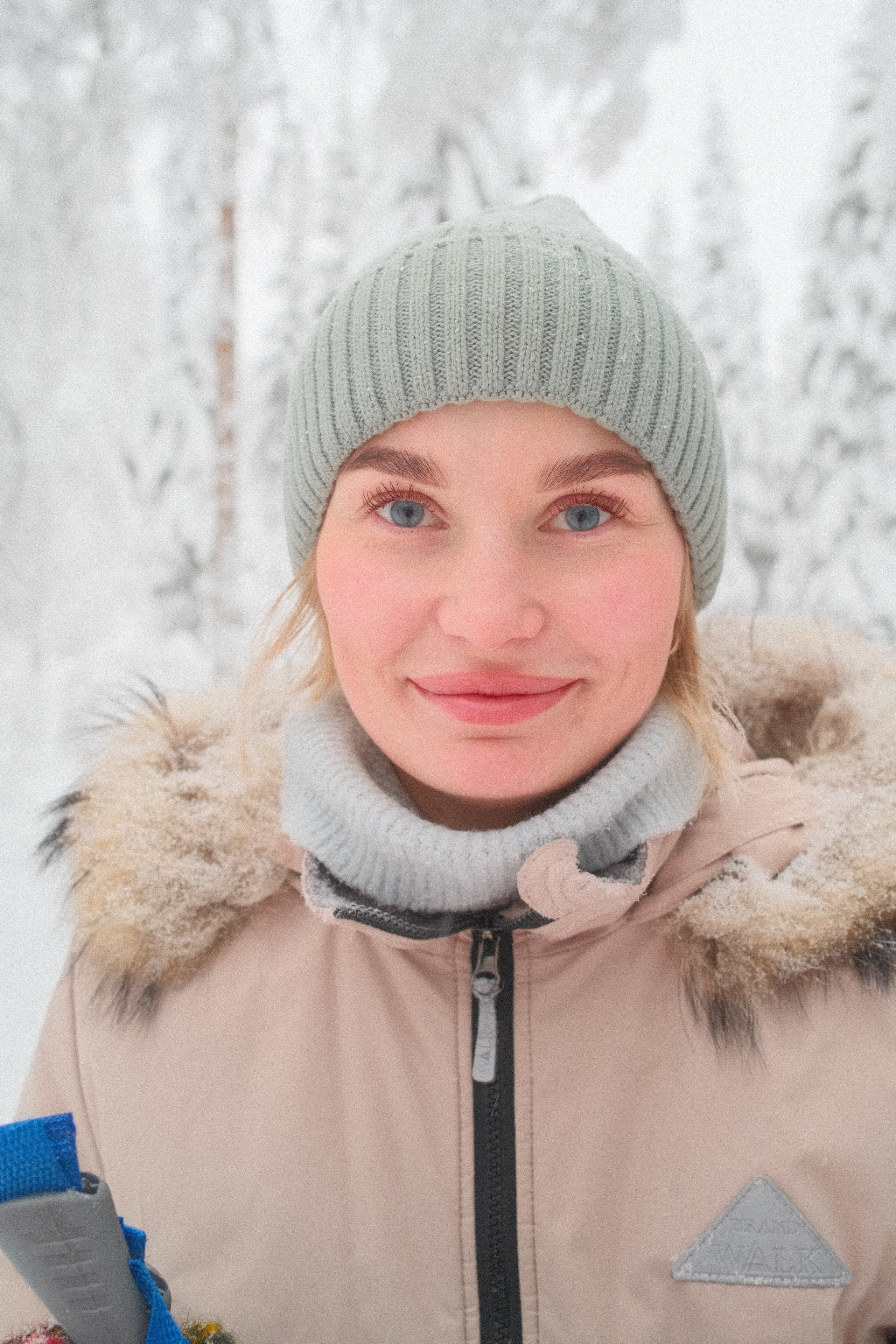 Портрет девушки с голубыми глазами в вязаной шапке в зимнем лесу