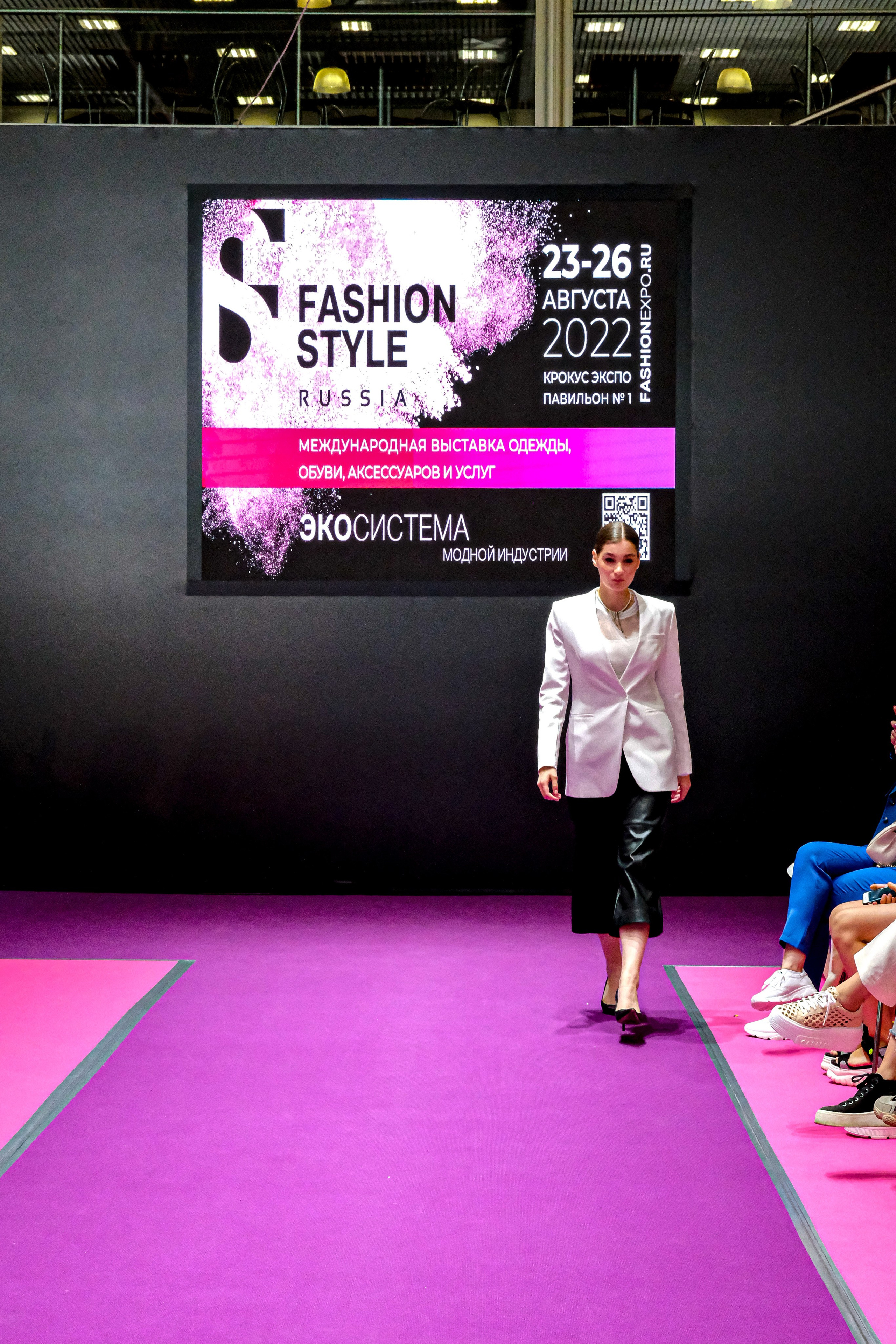  "Модели в ярких нарядах проходят по подиуму во время показа мод, освещенные яркими софитами и окруженные восторженными зрителями."