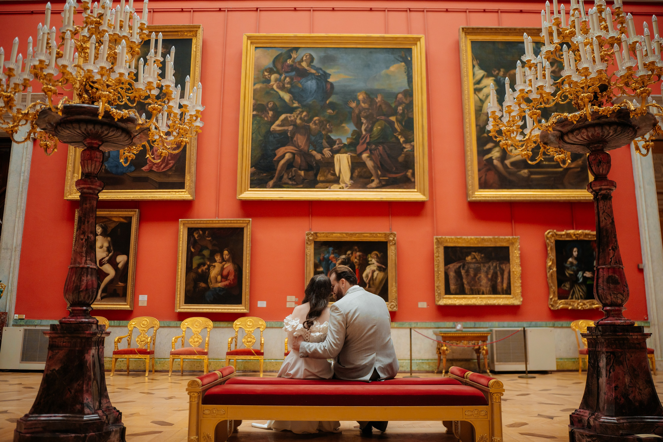 Свадебная фотосессия в Эрмитаже жених и невеста сидят на диване в красном зале и смотрят на картины