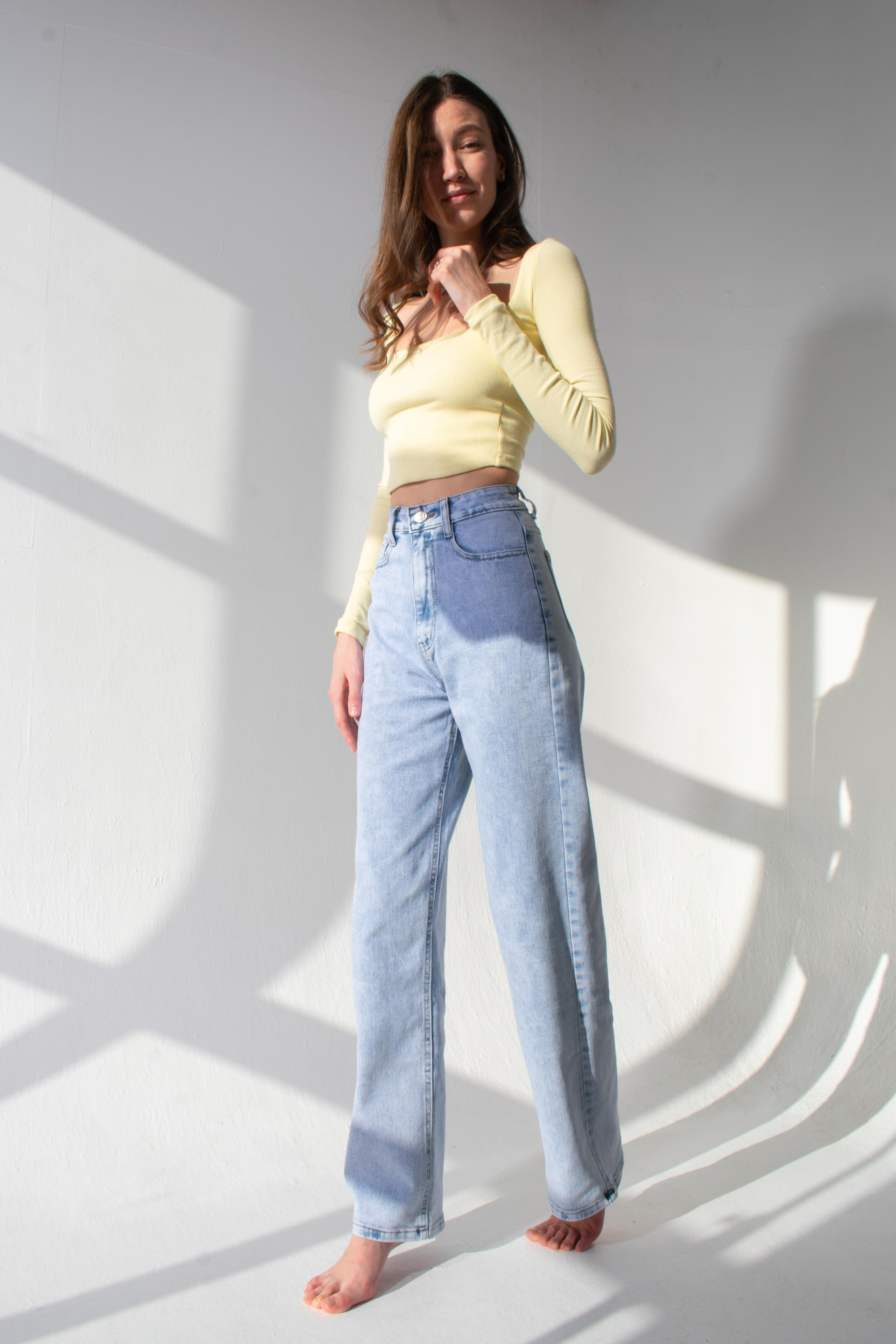 Модель фотографируется в солнечный день в студии в желтой футболке и джинсах