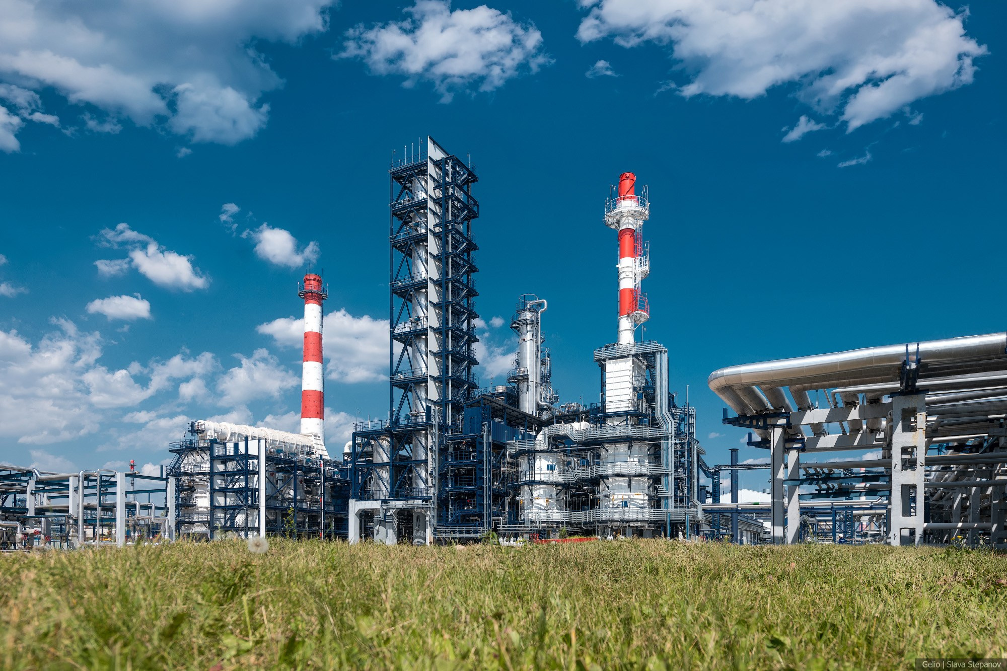 Современная нефтехимическая установка под ясным небом, блестящие серебристые ректификационные колонны и трубопроводы на фоне зелёной травы, фото Слава Степанов.