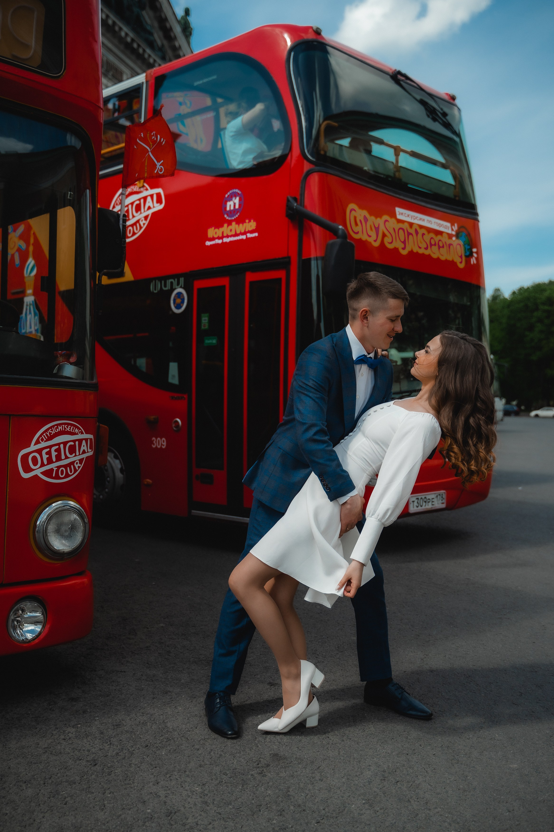 жених наклоняет в танце невесту на фоне красных туристических автобусов