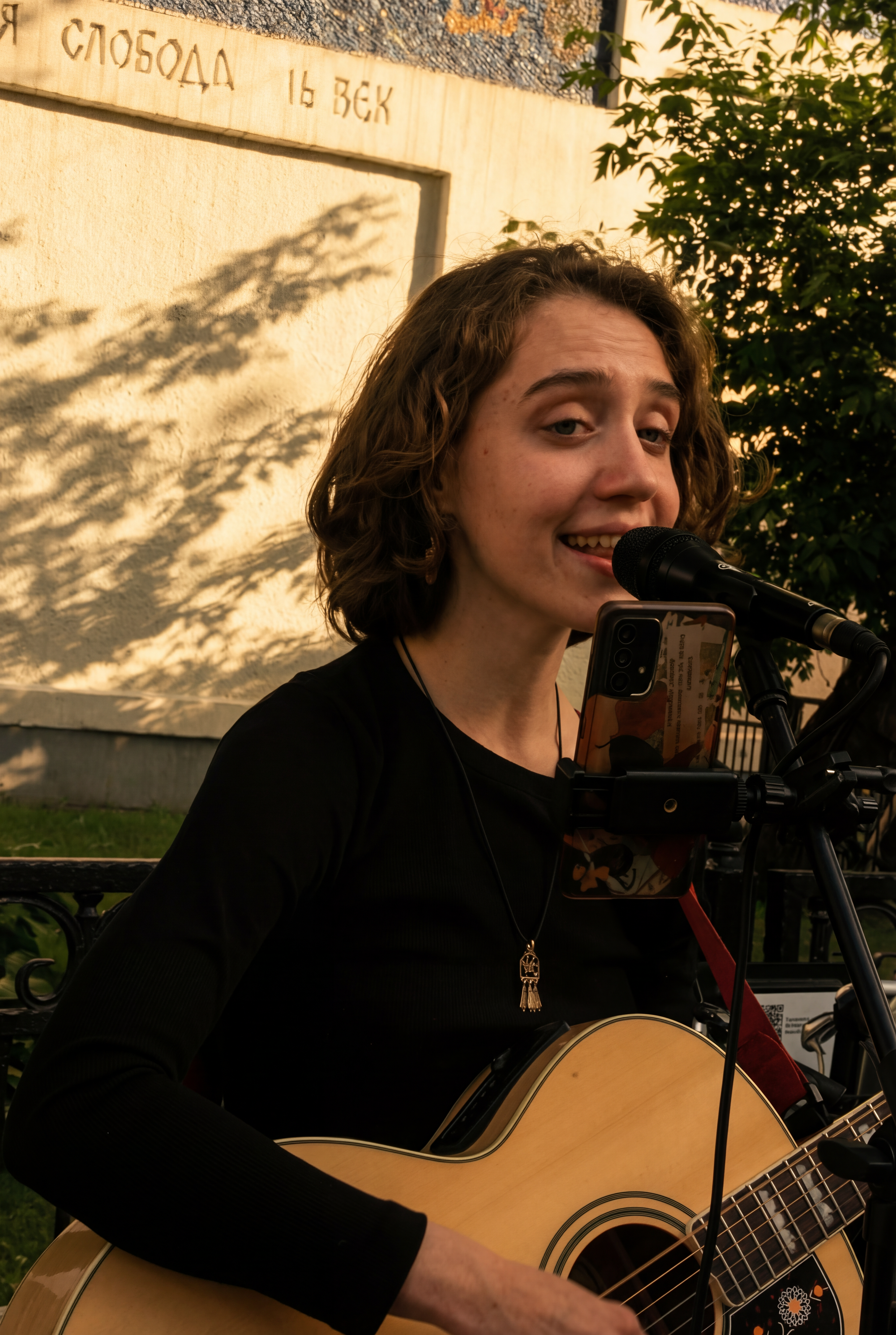 Портрет девушки на улице при естественном свете в действии, возле микрофона с гитарой