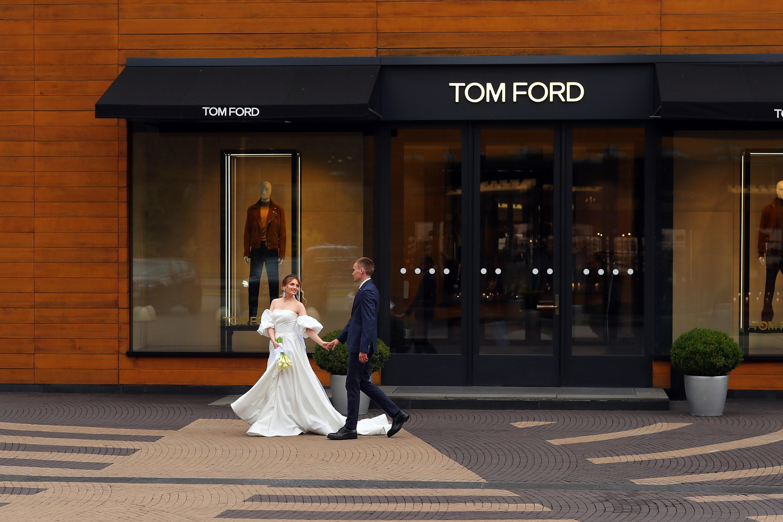 Жених с невестой прогуливаются на фоне магазинов.