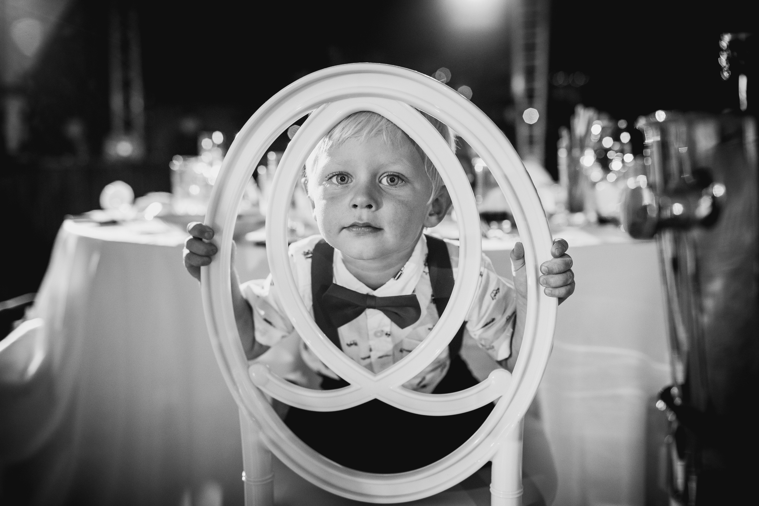 Маленький мальчик на свадьбе смотрит через спинку стула